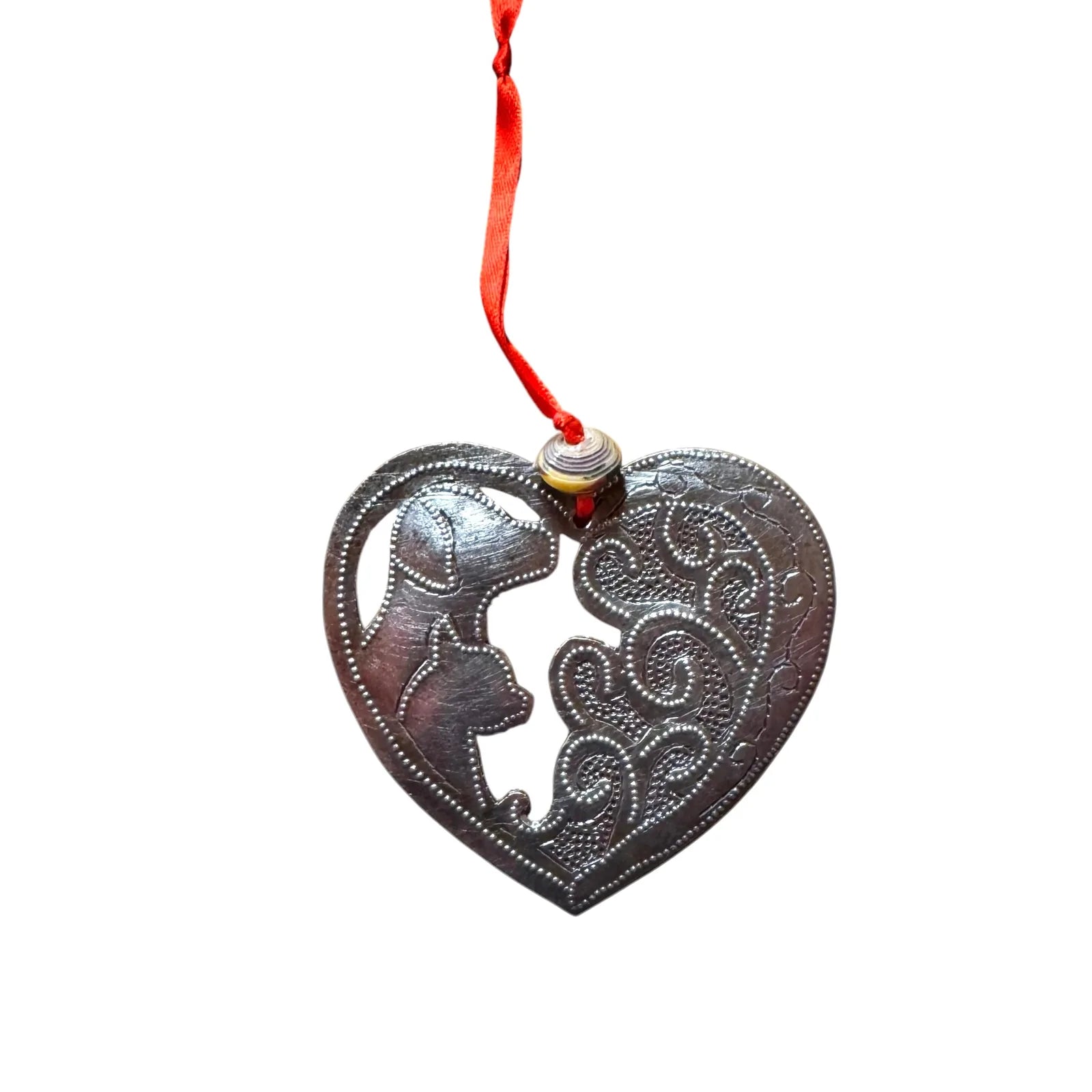 Heart-shaped metal ornament featuring dog silhouettes and intricate designs, hanging from a red ribbon.