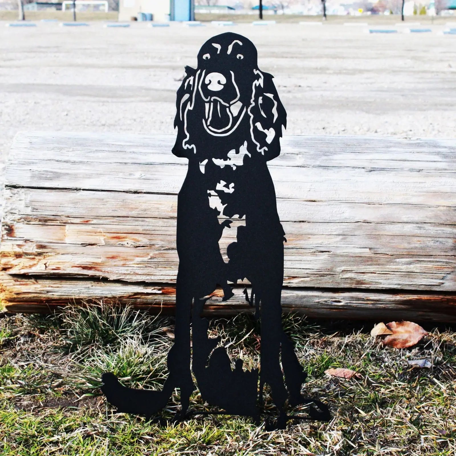 Black metal silhouette of an Irish Setter, showcasing intricate cutouts, placed on grassy ground near a log.
