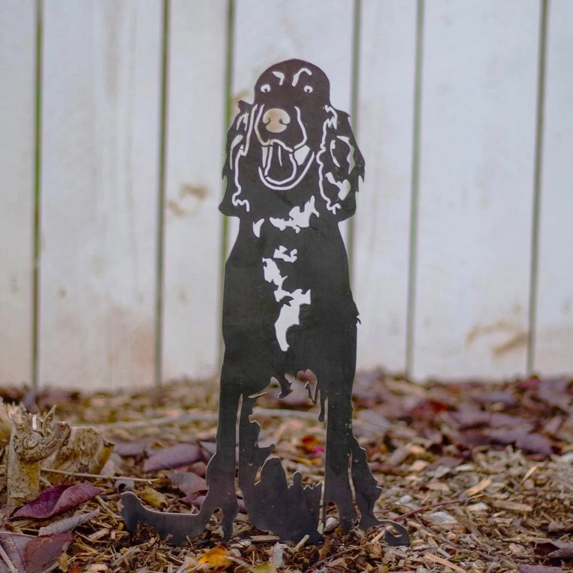 Irish Setter metal silhouette in matte black, standing in mulch with a rustic wooden background. Perfect outdoor dog decor.