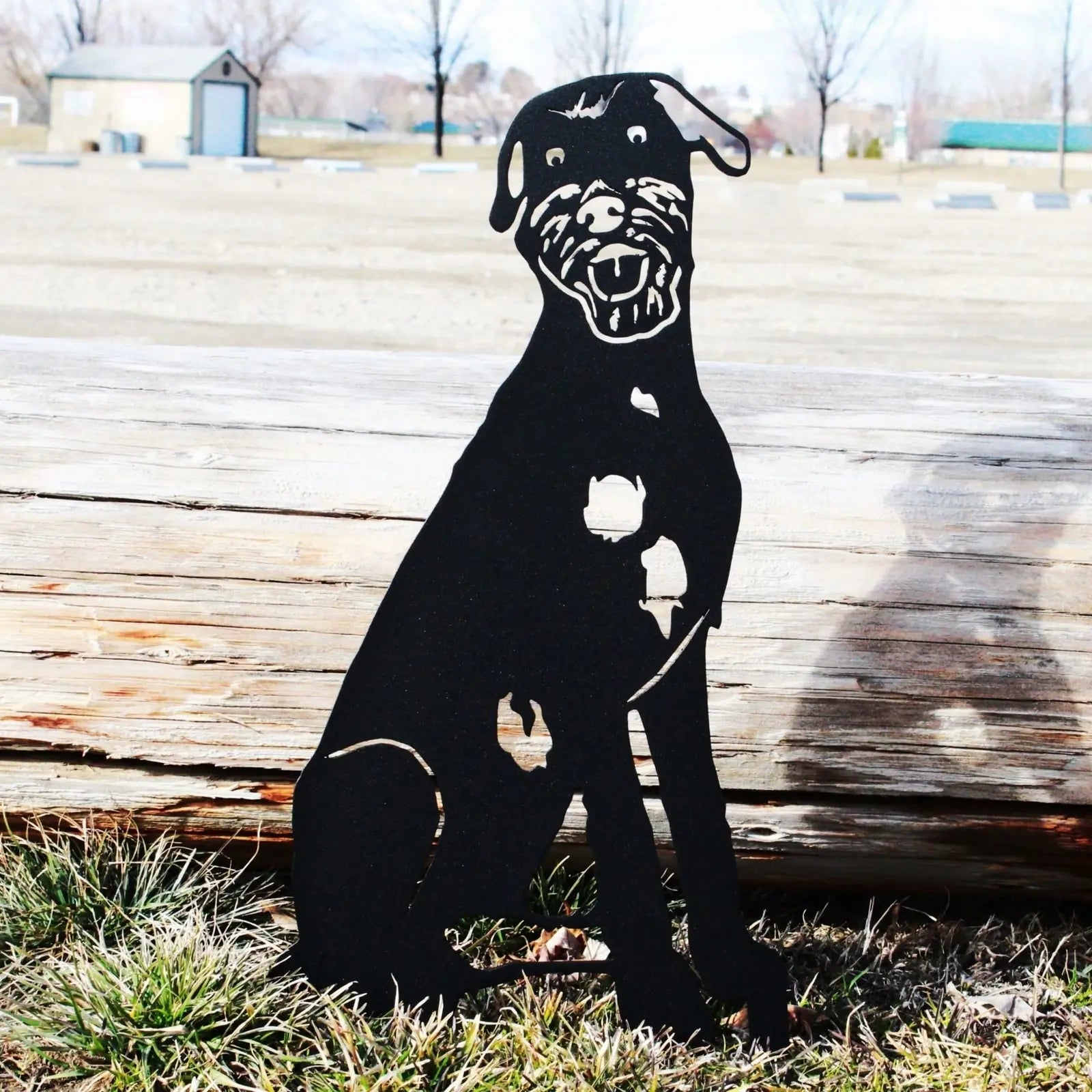 Black metal silhouette of an Irish Wolfhound sitting beside a wooden log, showcasing intricate detailing and outdoor decor.
