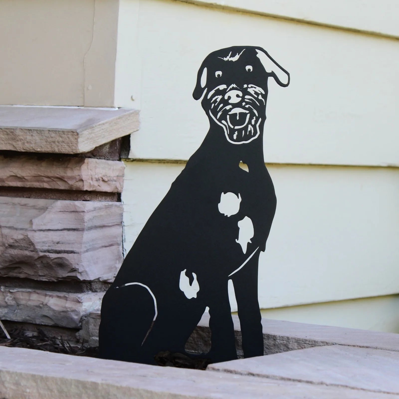Black metal silhouette of a dog sitting against a light-colored wall, showcasing white markings on its side.