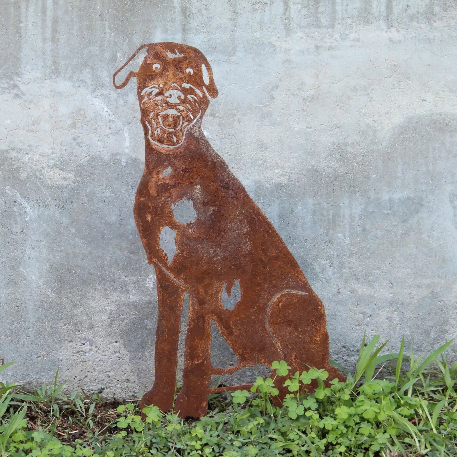 Rust-colored Irish Wolfhound metal silhouette displayed outdoors, blending with the garden's greenery and concrete backgro...