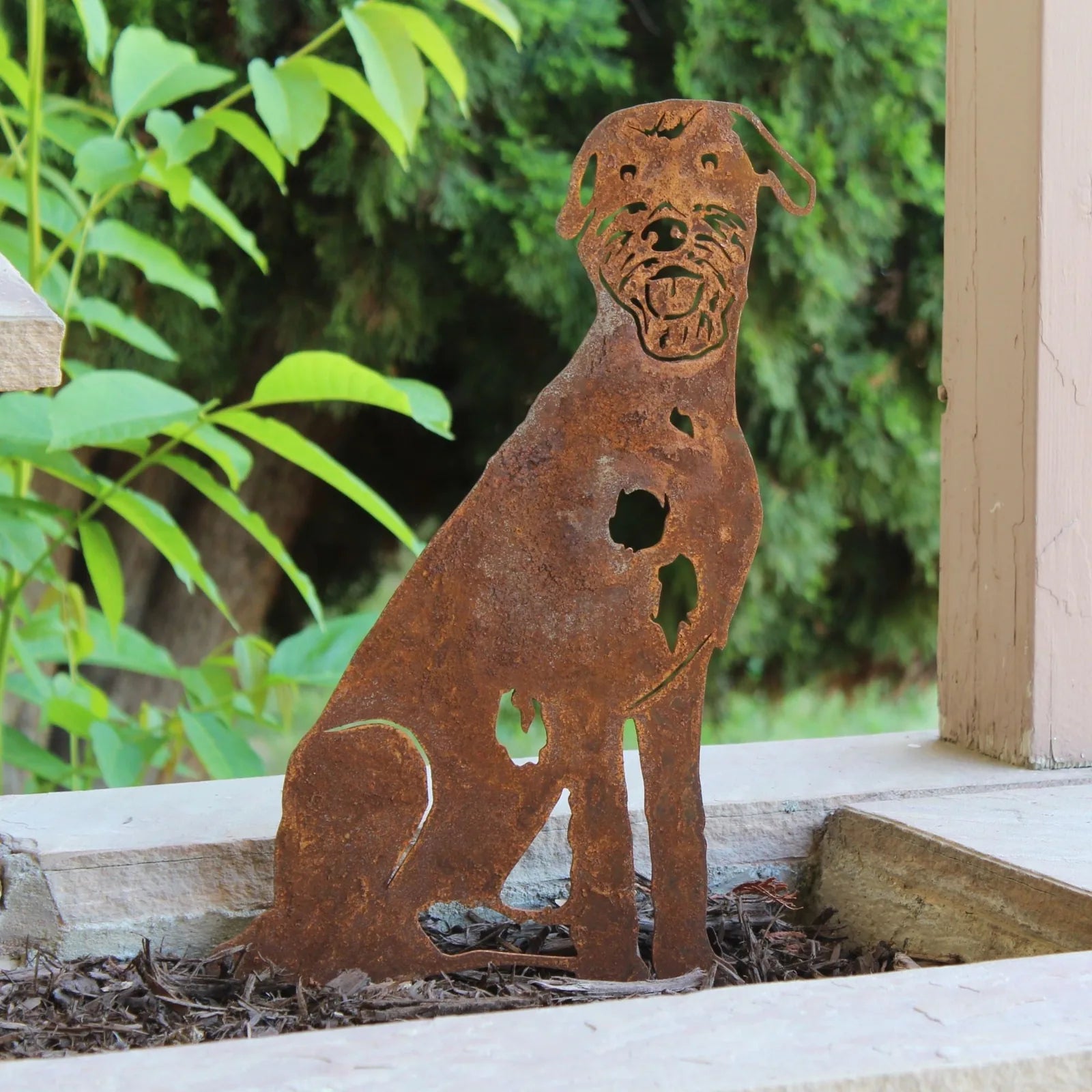 Rusty metal silhouette of an Irish Wolfhound, featuring cut-out details, set in a garden backdrop.