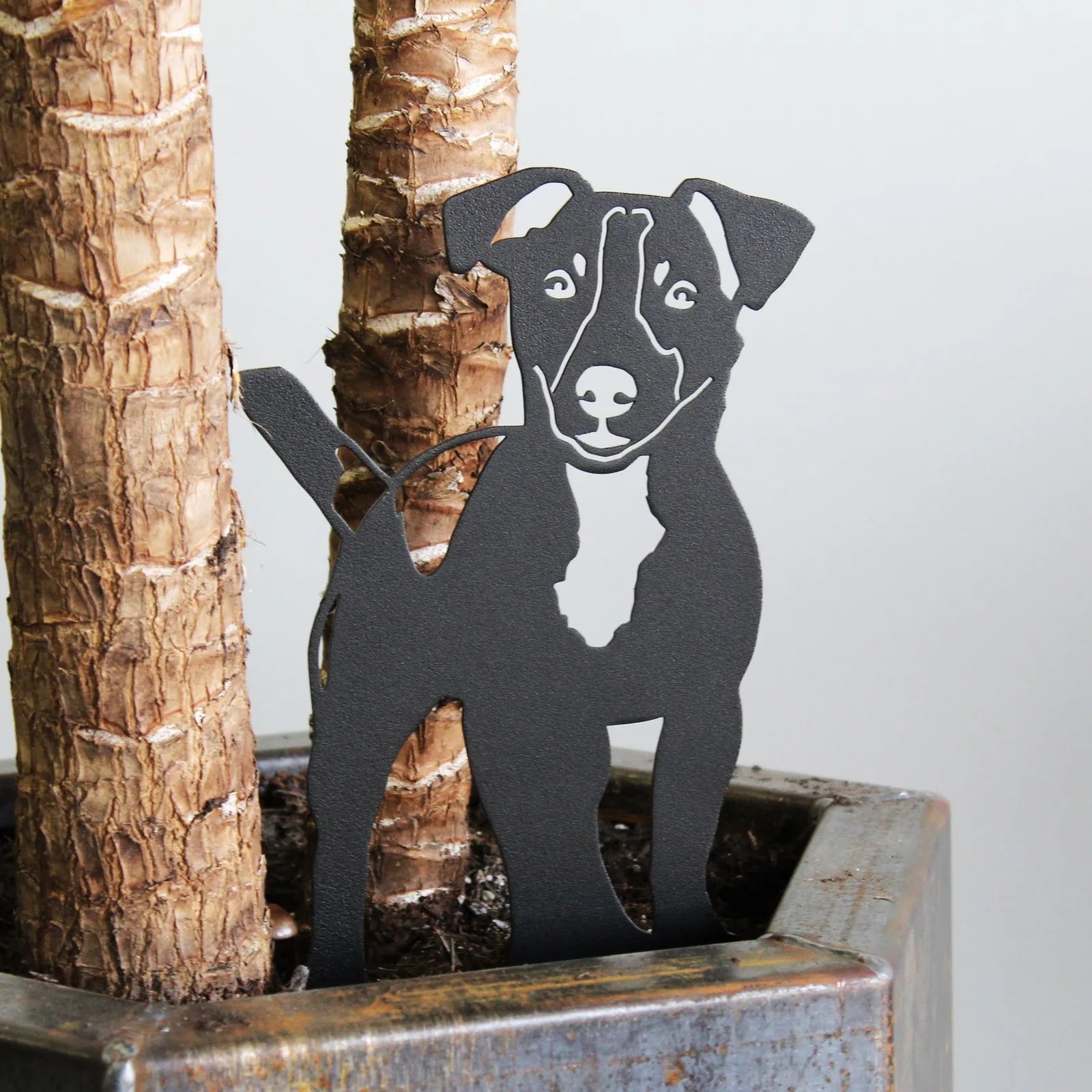 Black metal silhouette of a dog standing beside a plant pot, showcasing its detailed features and playful stance.