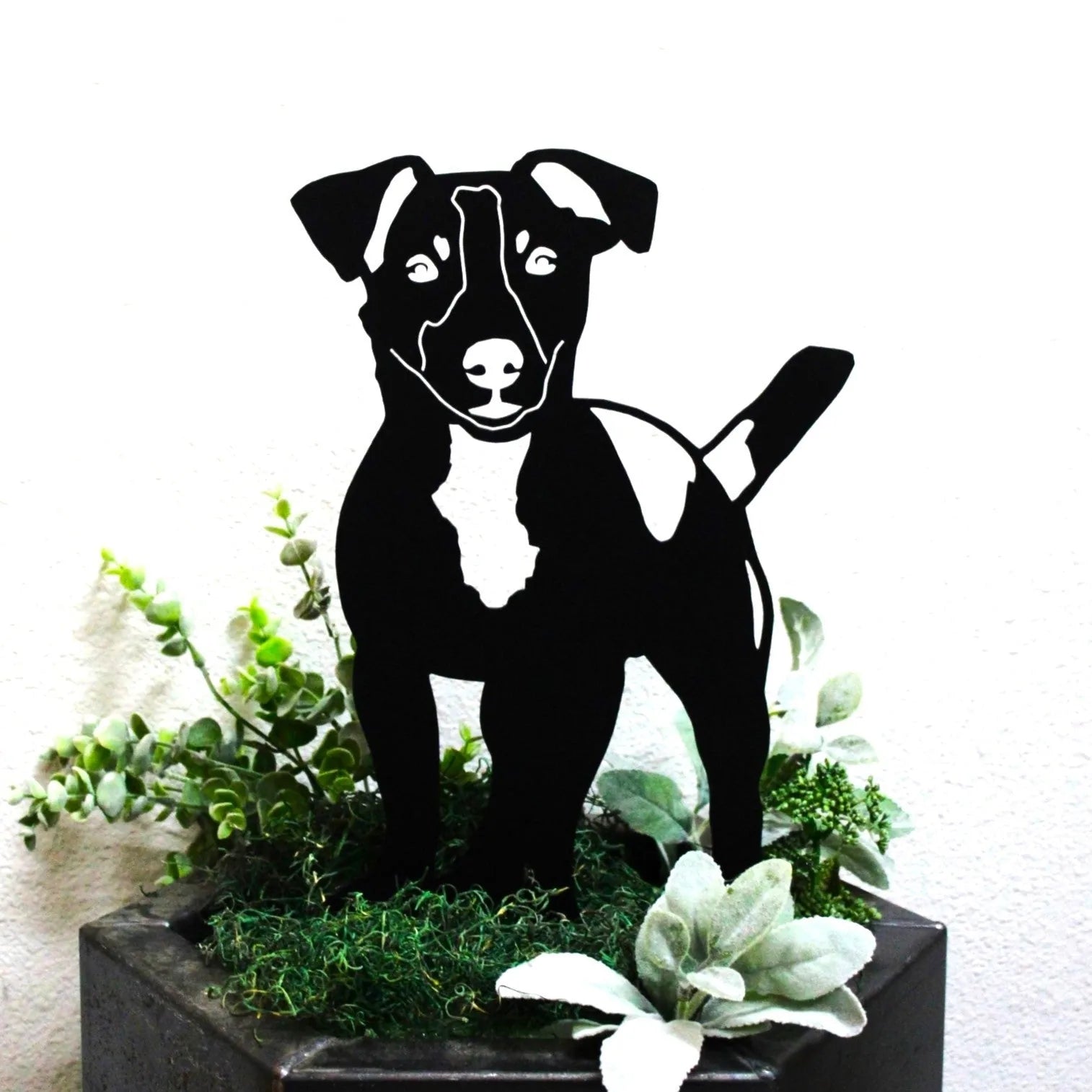 Black Jack Russell Terrier silhouette made of metal, surrounded by greenery in a decorative planter.