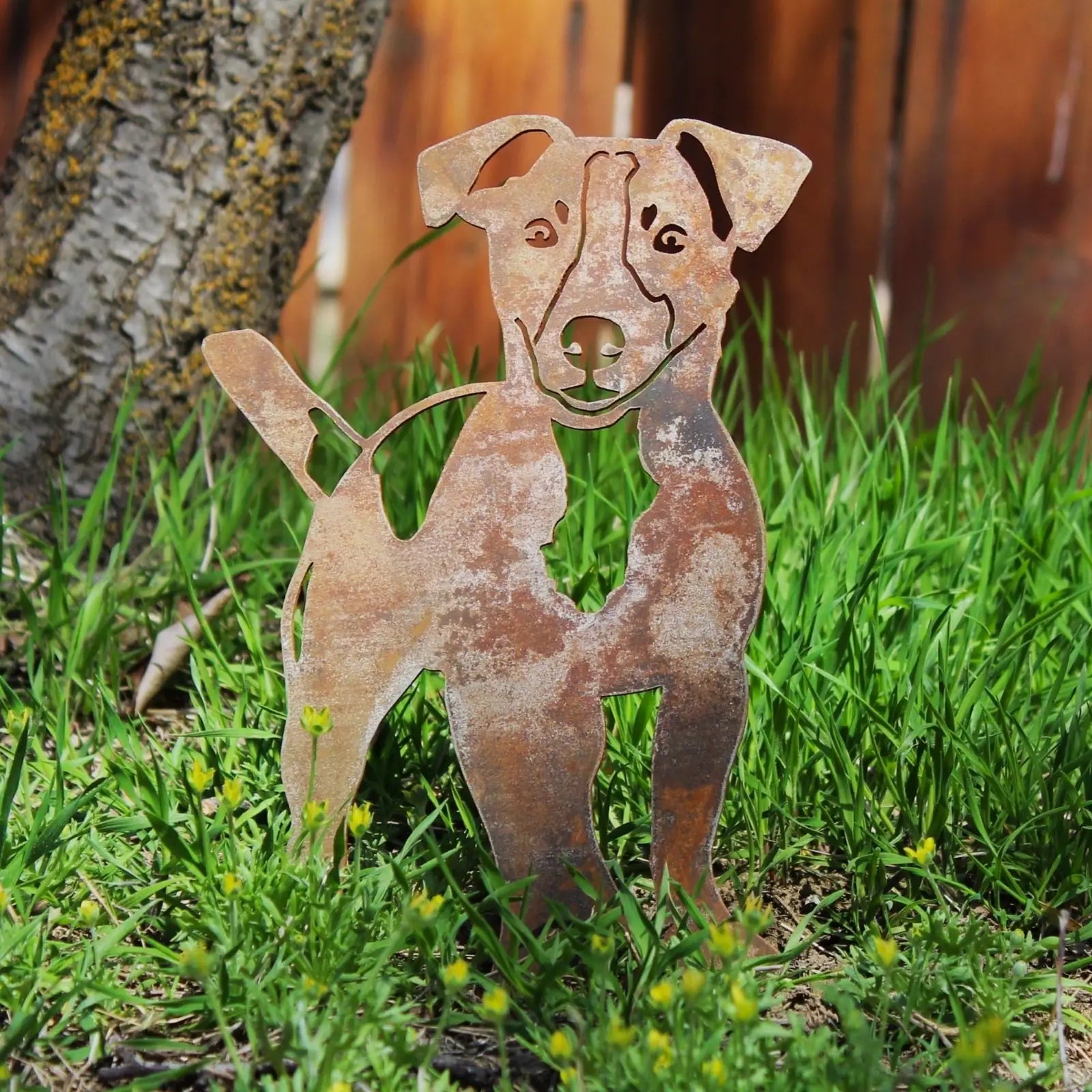 Rustic Jack Russell Terrier metal silhouette in Corten steel, standing among green grass, perfect for outdoor decor.