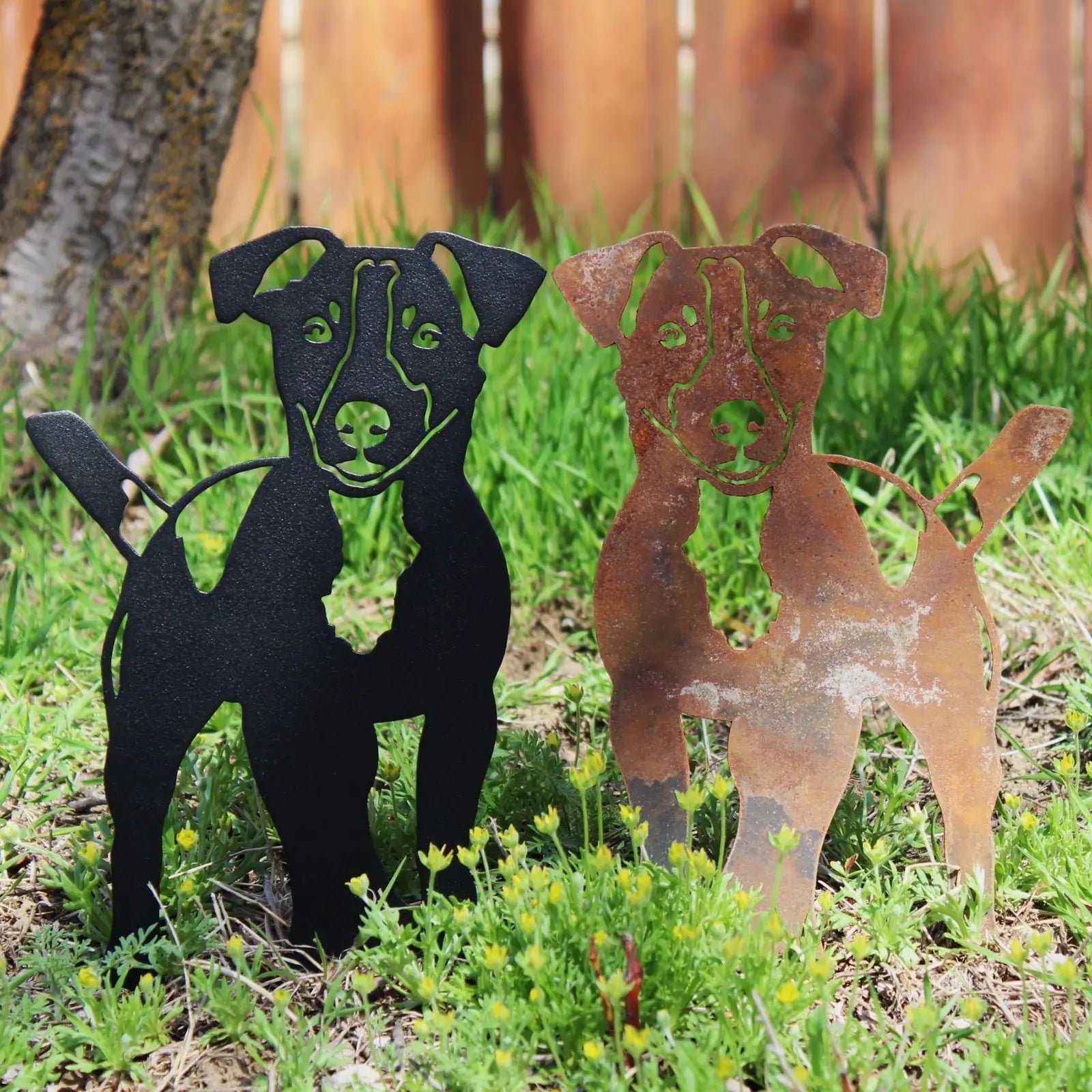 Jack Russell Terrier metal silhouettes in black and weathered Corten steel, set against green grass.
