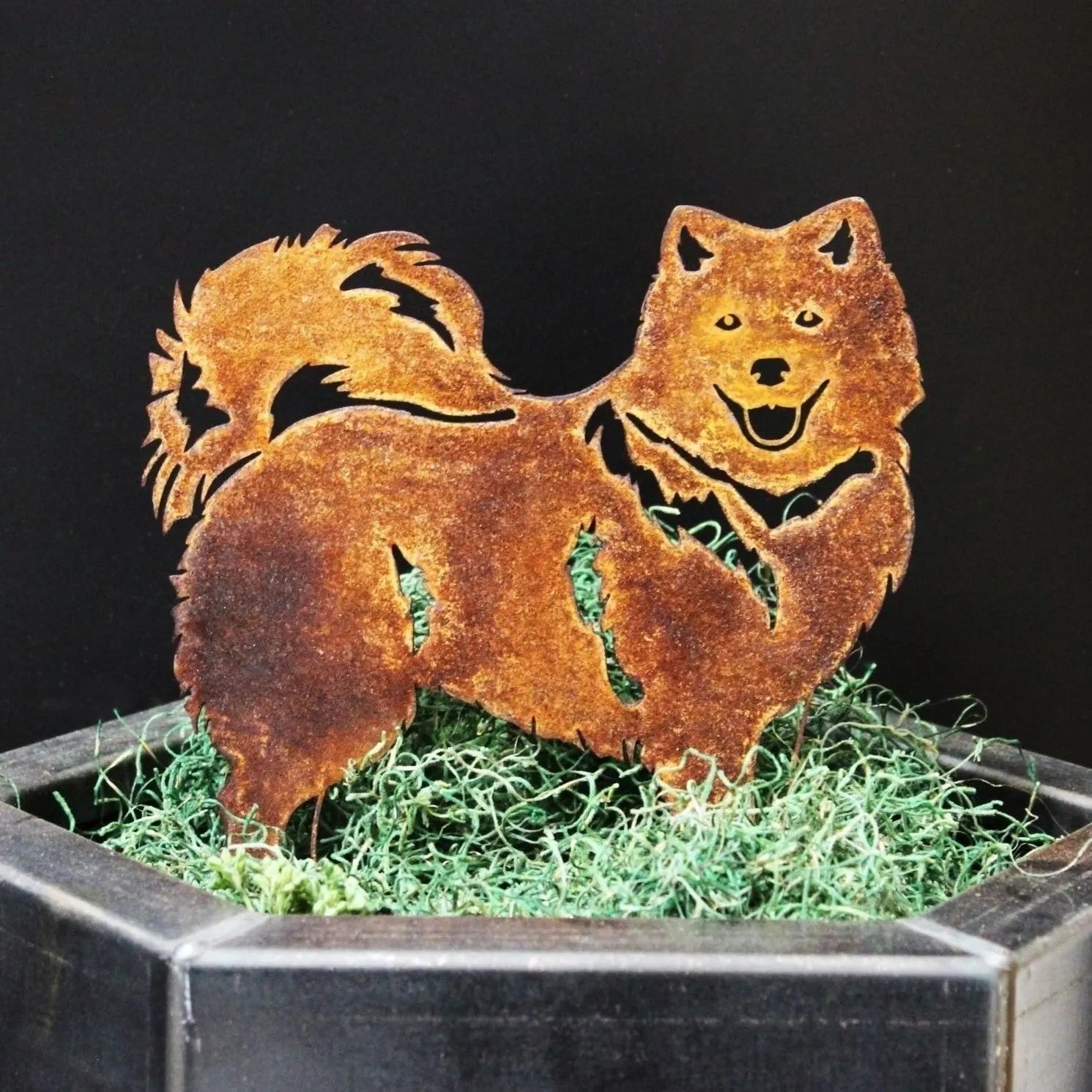 Japanese Spitz metal silhouette in rusted Corten steel, displaying a playful dog design among green grass in a planter.