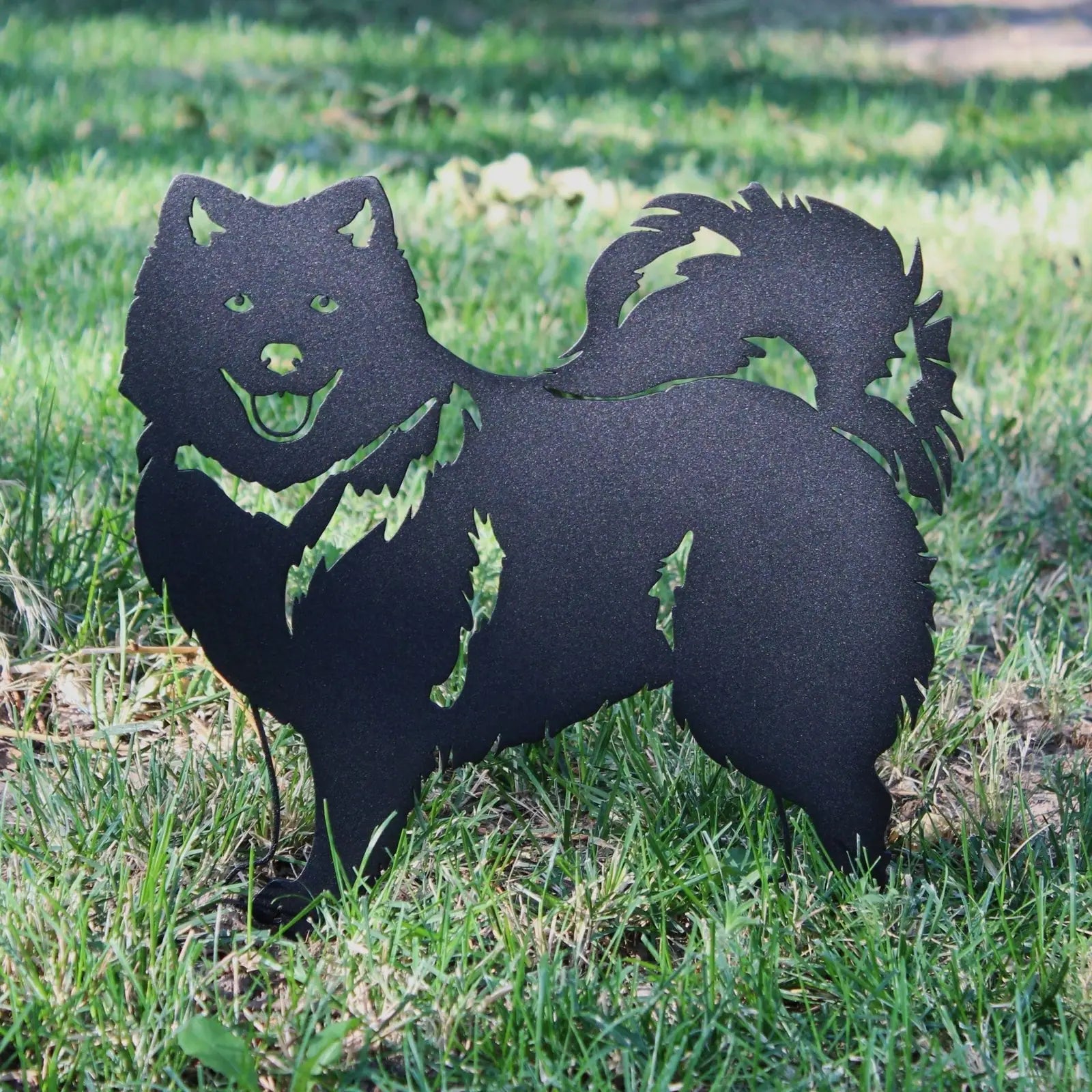 Keeshond silhouette in matte black metal, featuring detailed cutouts, displayed on green grass.