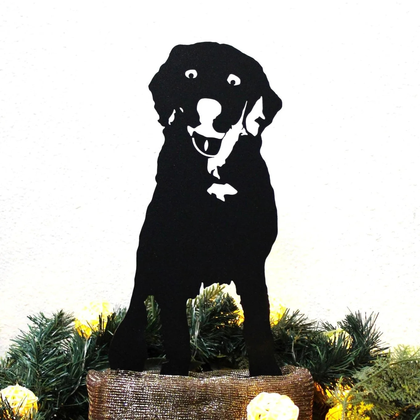 Black metal silhouette of a Labrador Retriever, smiling, displayed among greenery and lights.