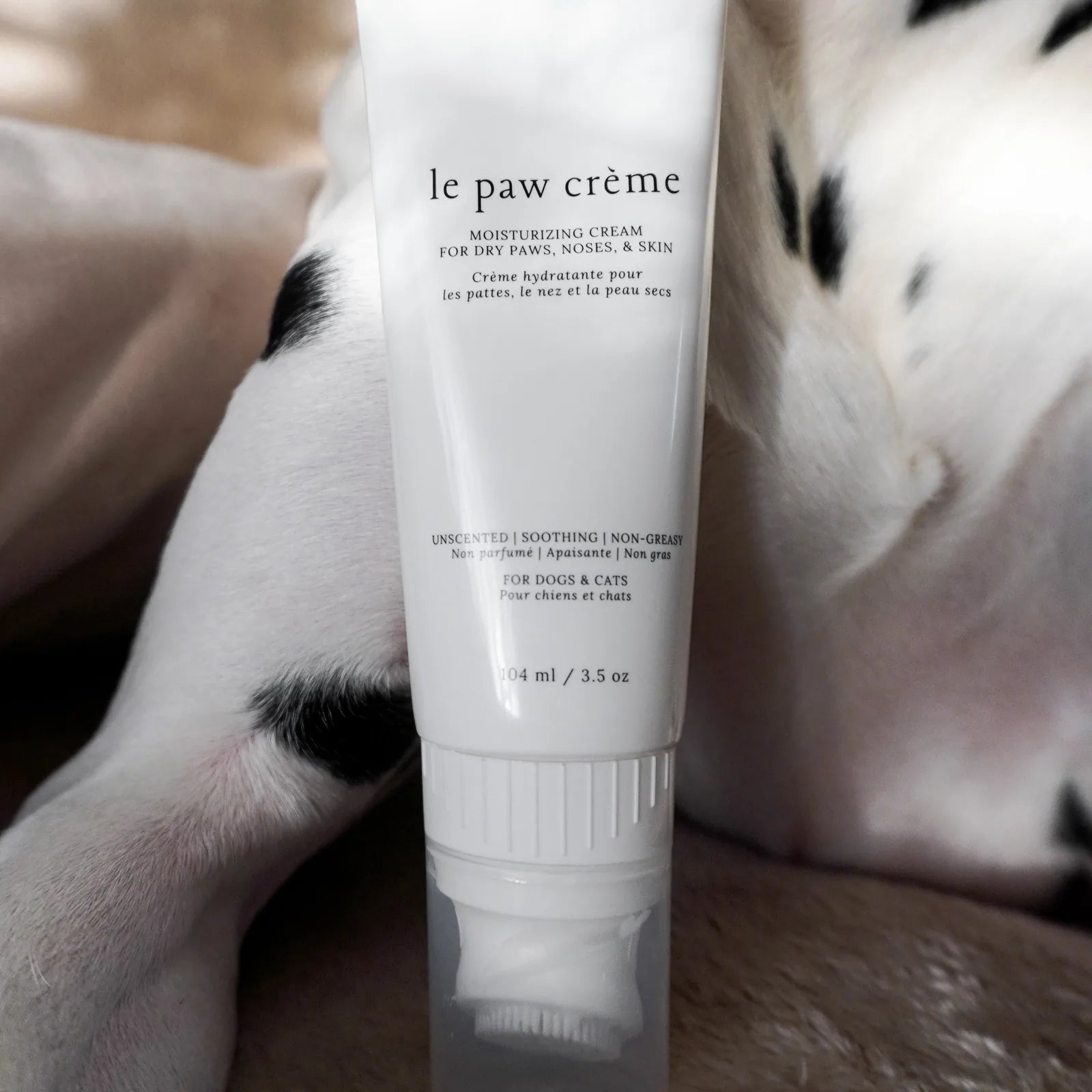 Le Paw Crème in a white tube, designed for moisturizing pets' dry paws, resting on a soft surface near a dog's paw.