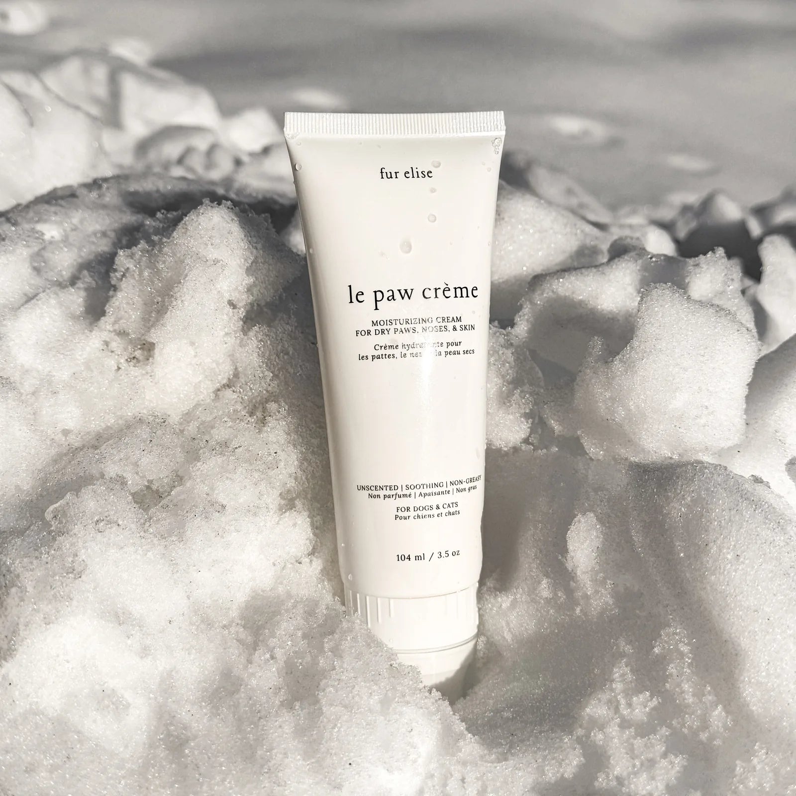 Le Paw Crème tube nestled in soft snow, showcasing a sleek white design and clear labeling for moisturizing pet care.