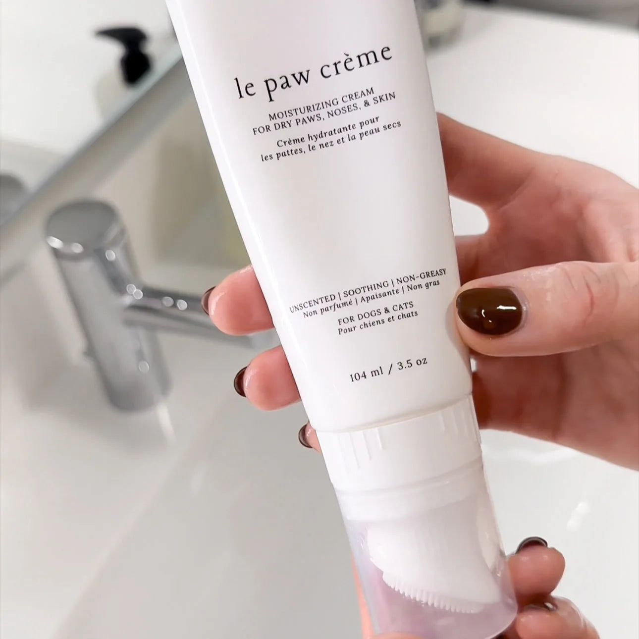 Le Paw Crème tube held in hand, featuring a white design and silicone bristle applicator for easy use on pets' paws.