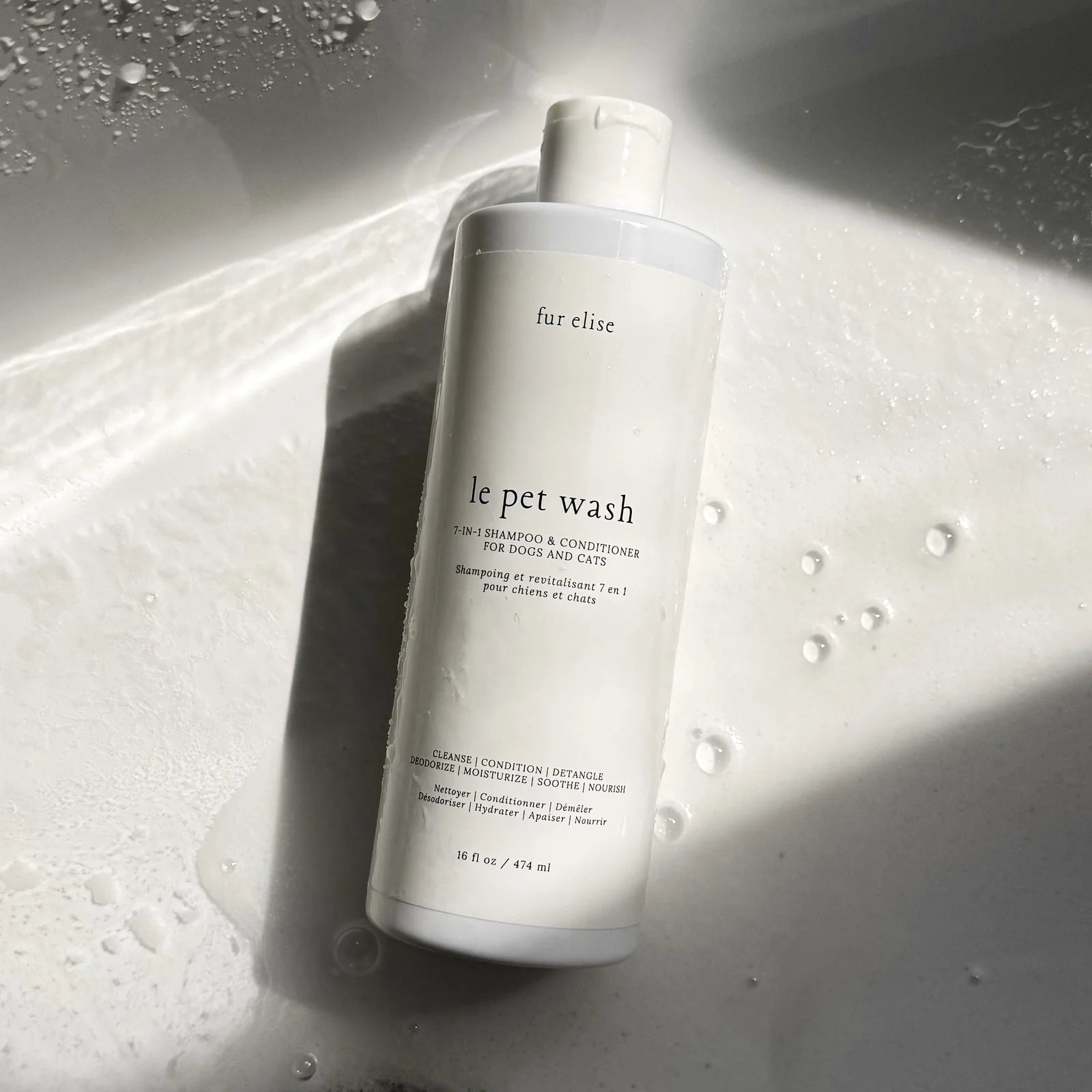 Le Pet Wash bottle in a wet sink, displaying a simple white design with black text and a disc top cap, surrounded by bubbles.