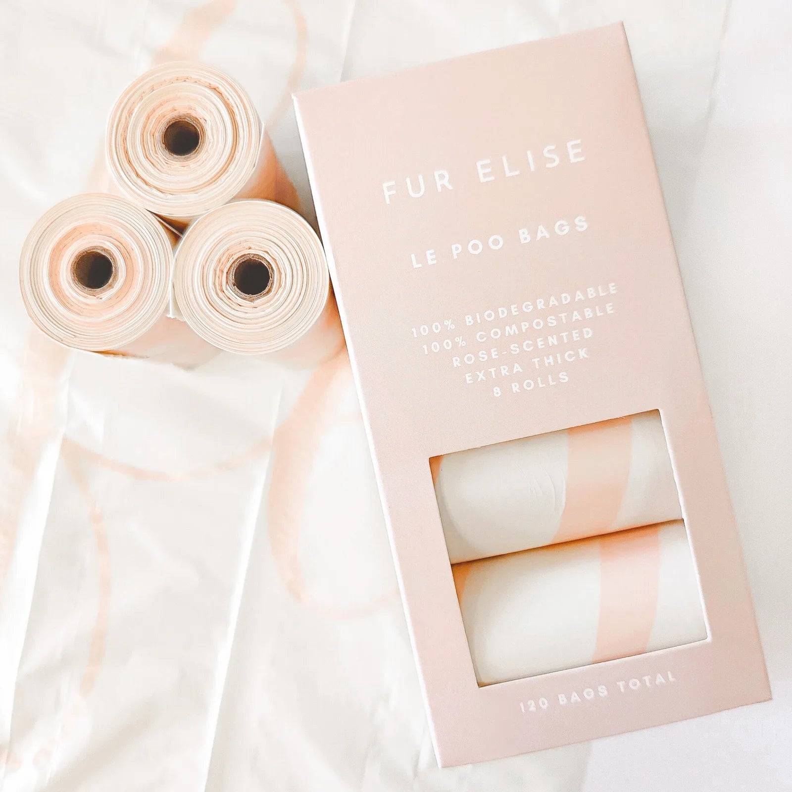 Le Poo Bags by Elise Galleria, featuring light pink rolls and a sleek box, are biodegradable and rose-scented for pet waste.