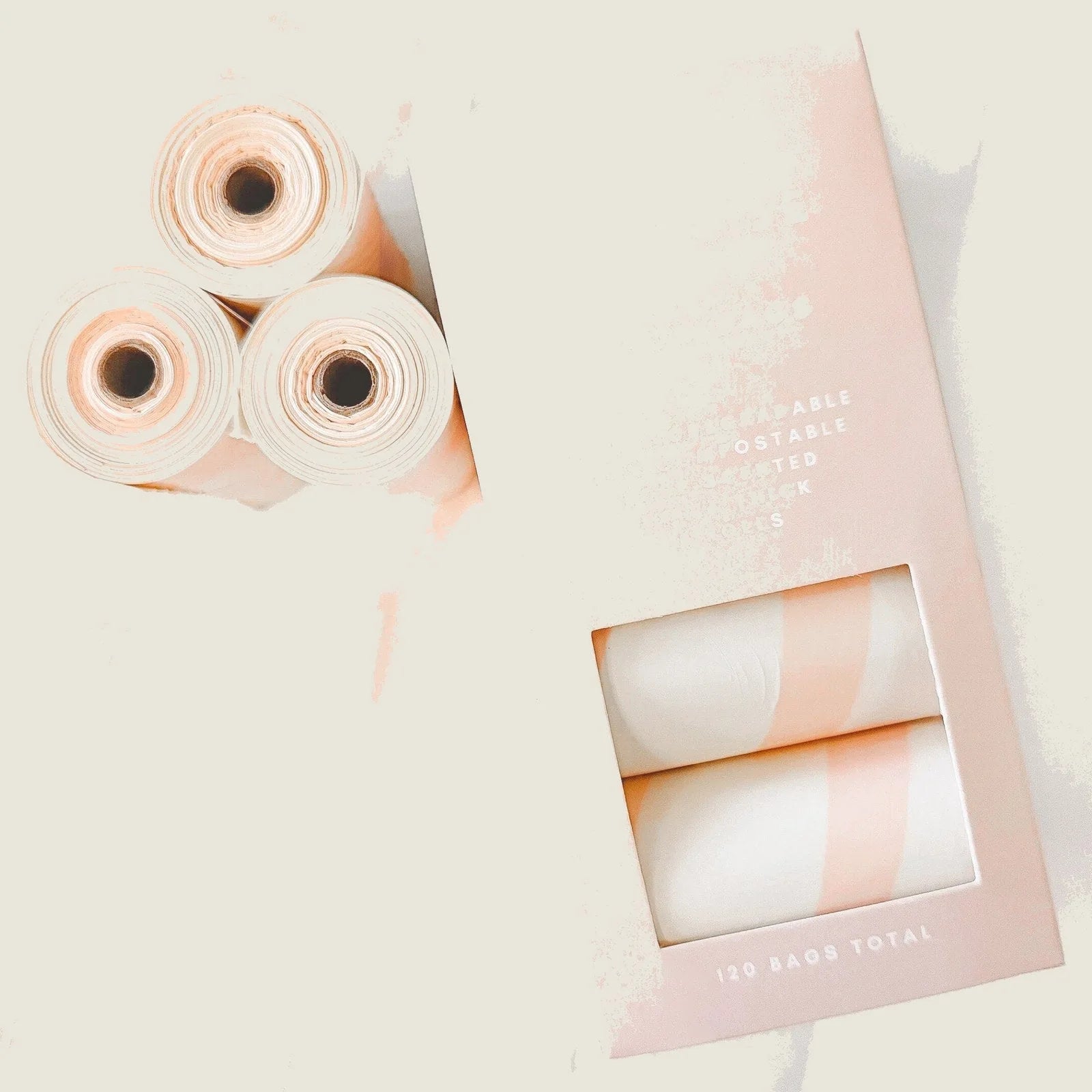 Biodegradable rose-scented dog waste bags in a soft peach packaging, showing three rolls inside a box with 120 bags total.
