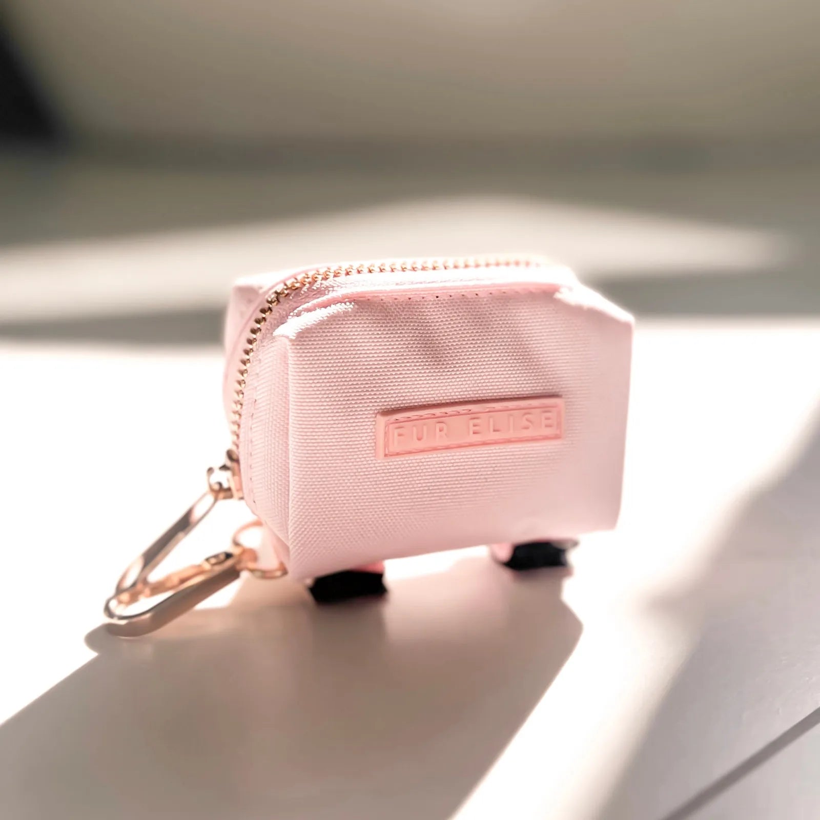 Pink Le Poo Pouch made of durable Oxford fabric, featuring a rose gold zipper and logo, with a clasp for easy attachment.