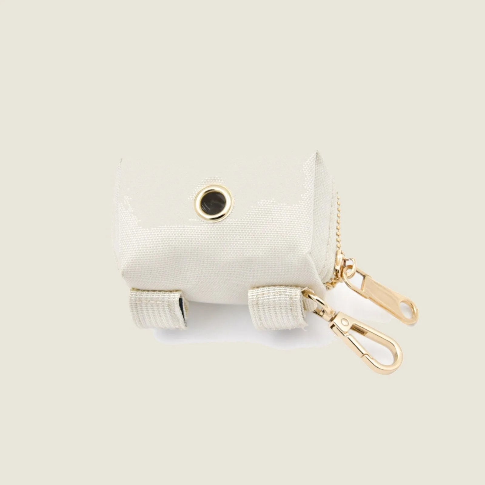 Cream-colored pet waste dispenser made of durable Oxford fabric with gold hardware and Velcro ties for leash attachment.