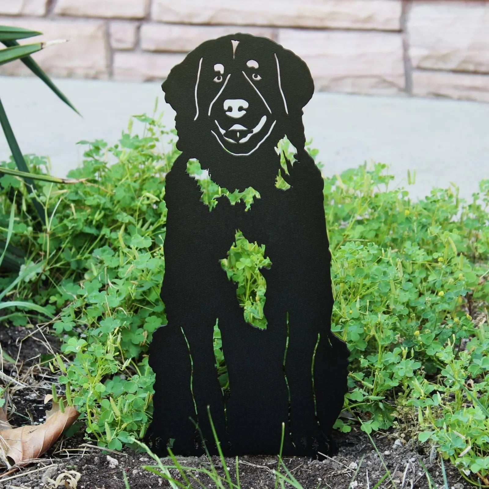 Black Leonberger metal silhouette art piece set among greenery, showcasing a playful dog design for outdoor decor.