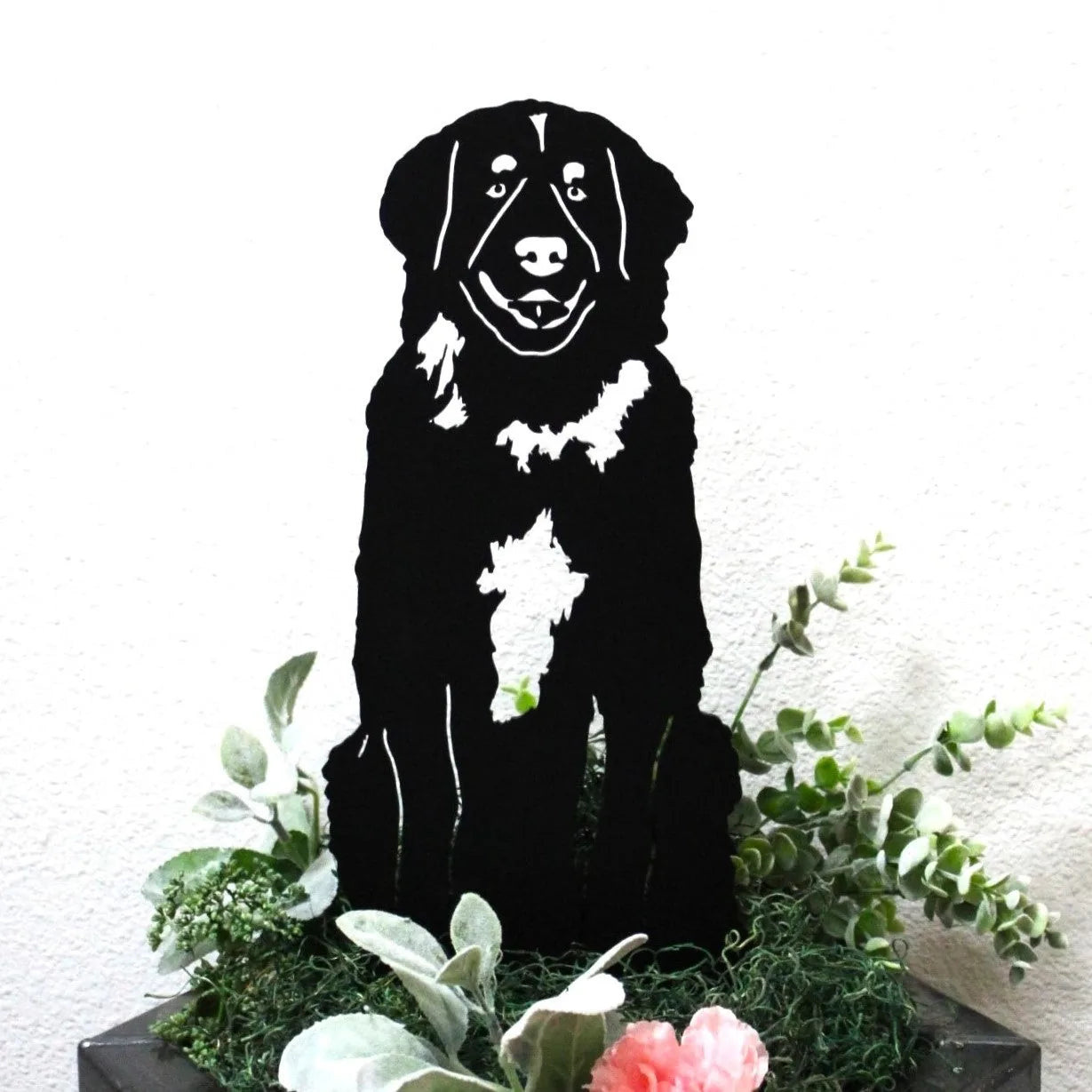 Black metal silhouette of a Leonberger dog among green foliage and floral accents, perfect for outdoor decor.
