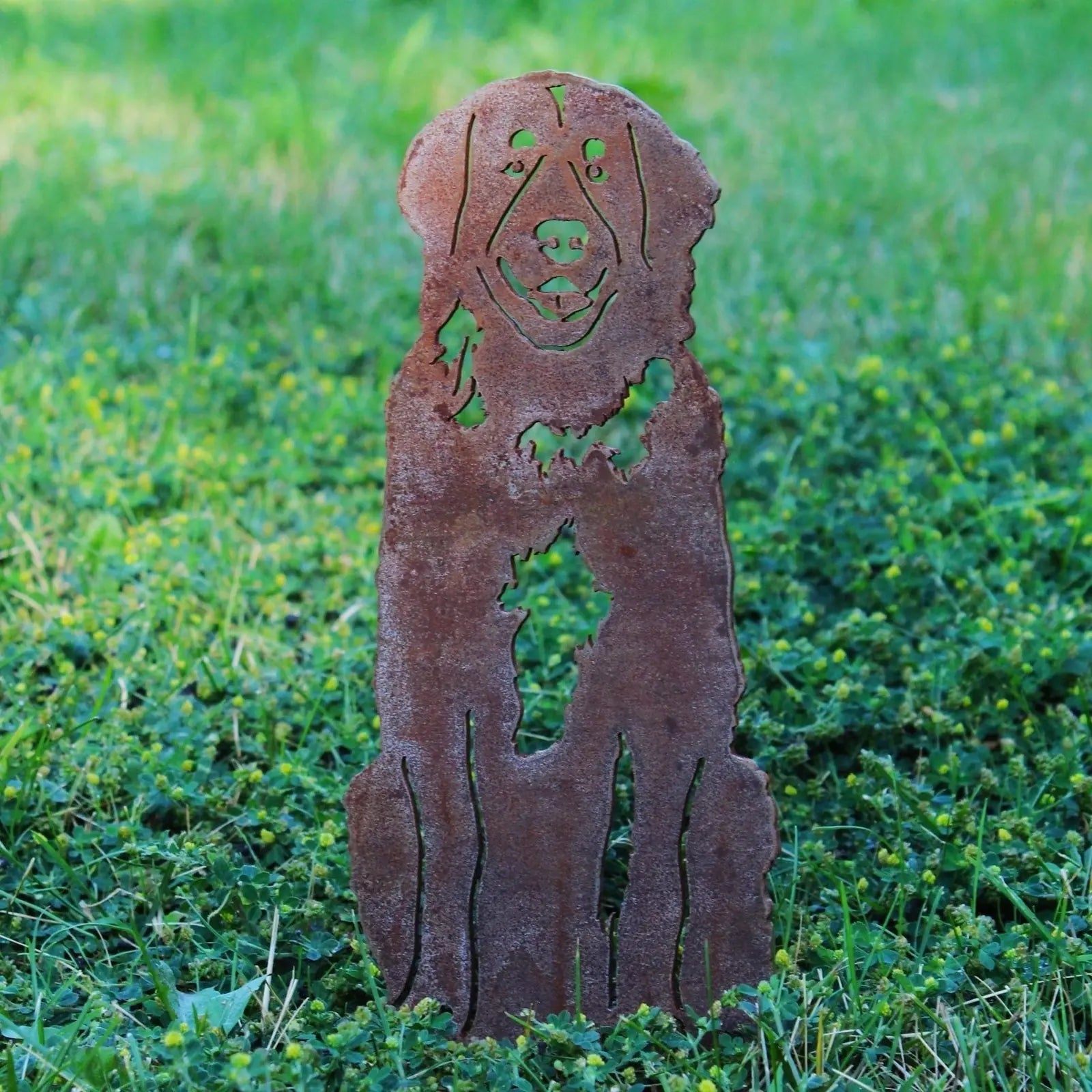Rusty metal silhouette of a Leonberger dog standing in green grass, showcasing intricate cut-out details.