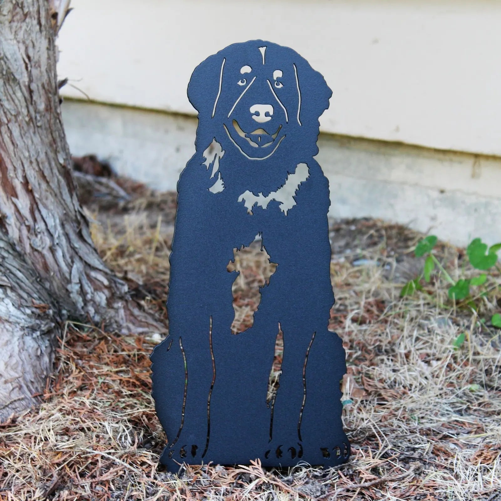 Black metal silhouette of a Leonberger dog, displayed outdoors among dry grass and tree roots, designed for garden decor.