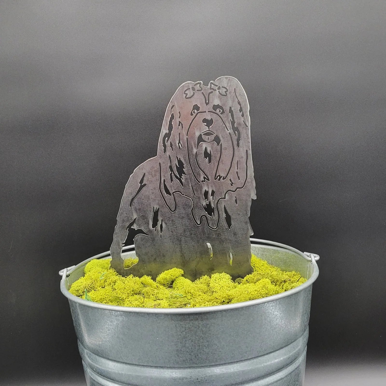Lhasa Apso metal silhouette in dark steel, displayed in a bucket filled with vibrant green moss.