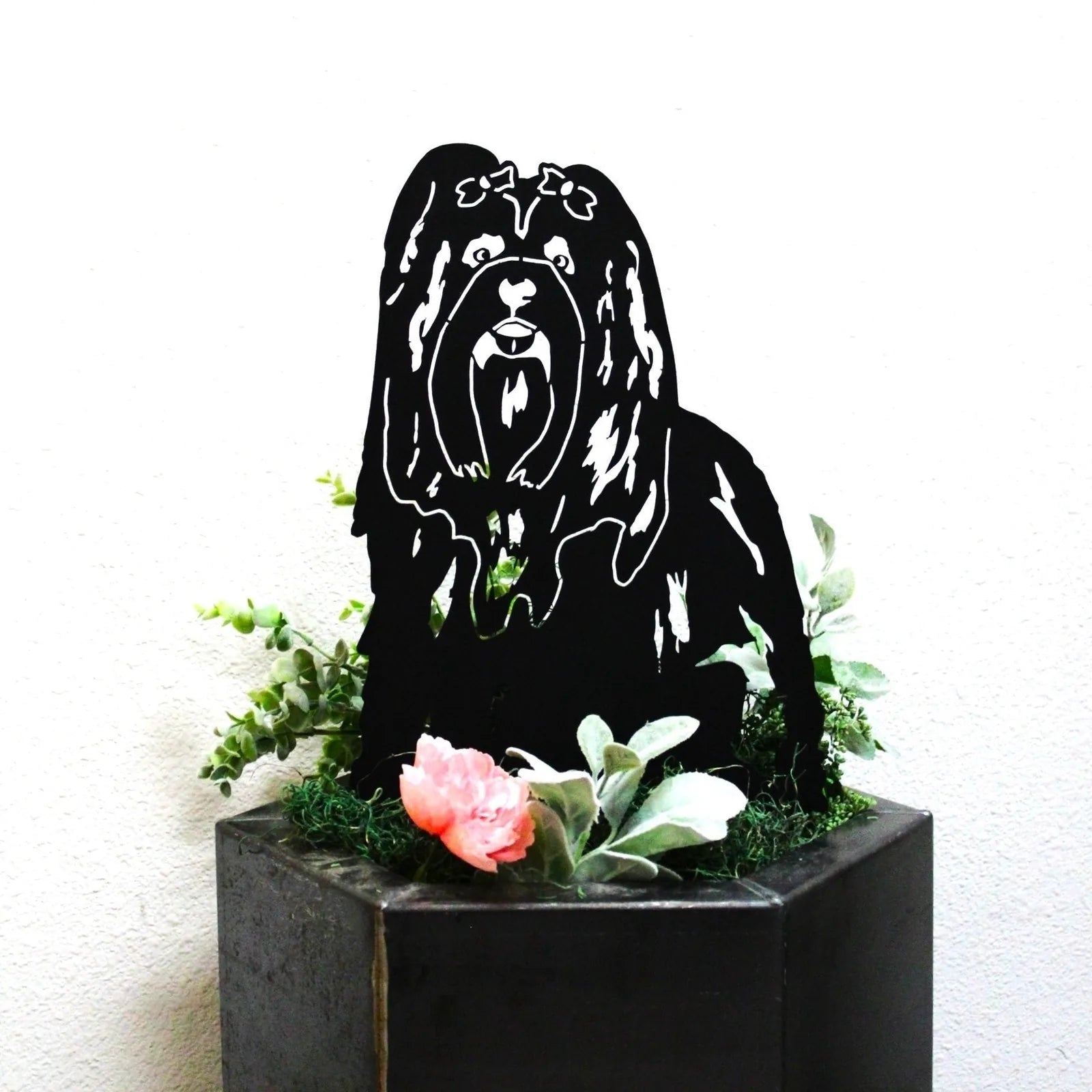 Black Lhasa Apso metal silhouette art, surrounded by greenery and flowers, ideal for outdoor decor.