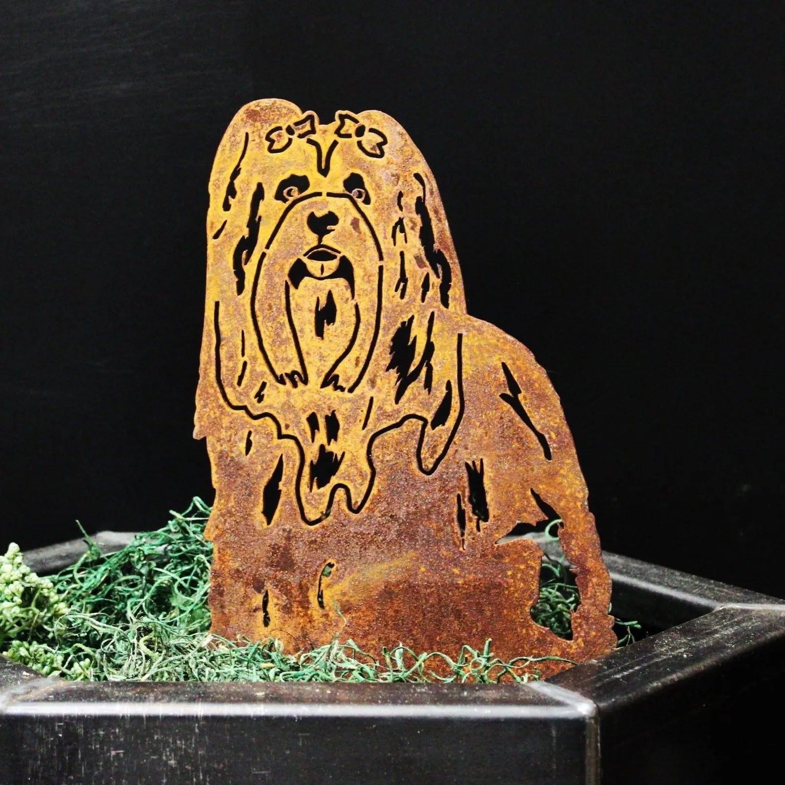 Rusty Lhasa Apso metal silhouette art, crafted from Corten steel, displayed among green moss in a black planter.