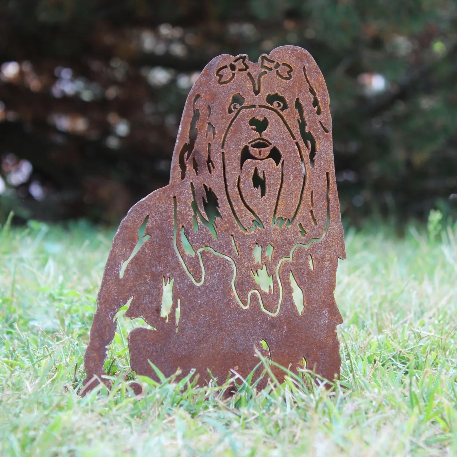 Lhasa Apso metal silhouette in weathered Corten steel, set against a grassy outdoor backdrop.
