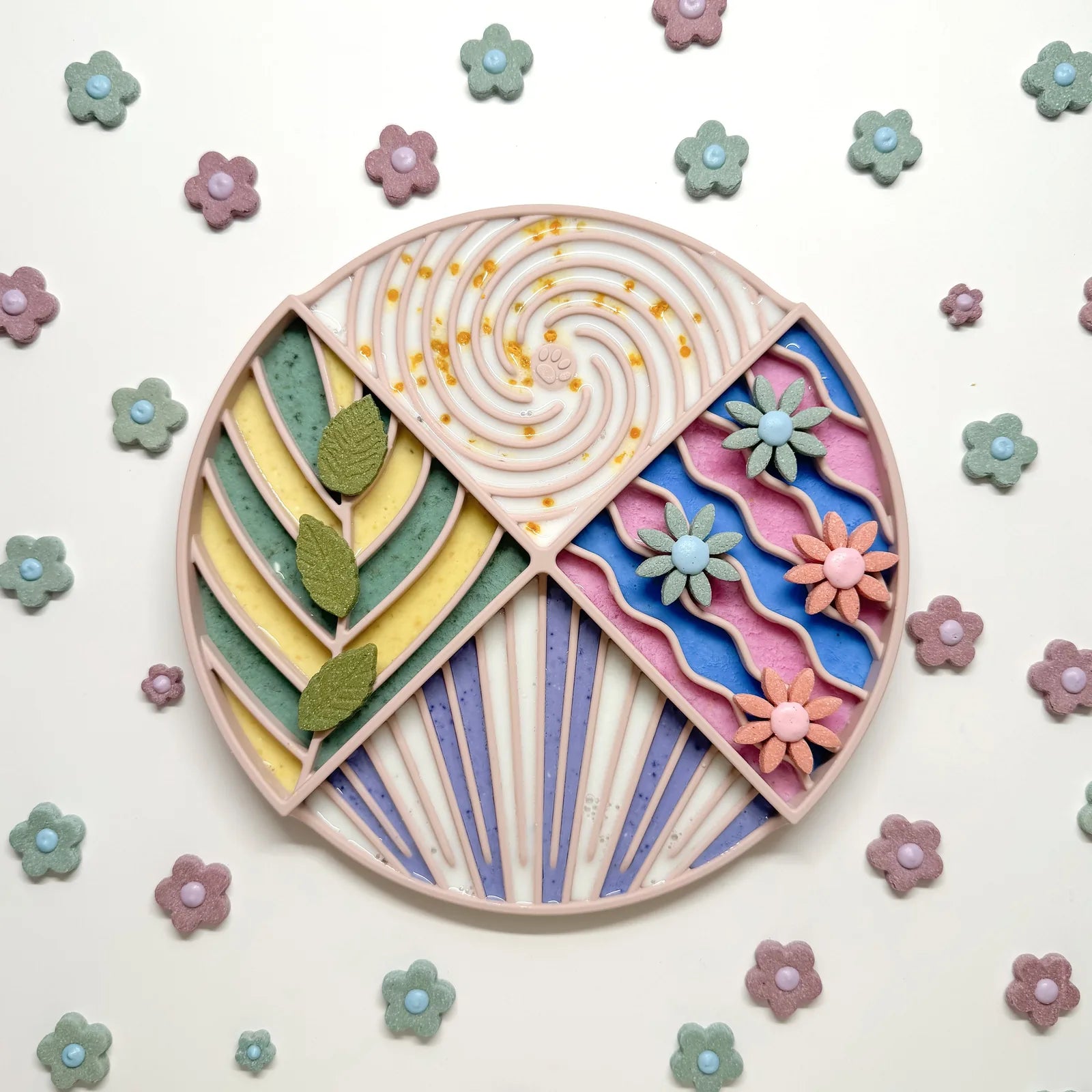 Colorful lick mat with a circle design, featuring patterns and leaf shapes, surrounded by flower-shaped treats.