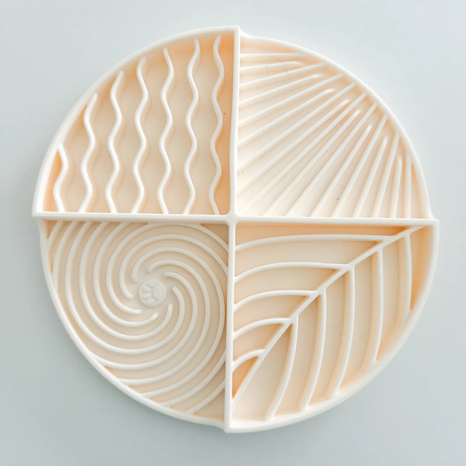 Light cream lick mat, circular shape, with four engaging textured sections for dog play and feeding.