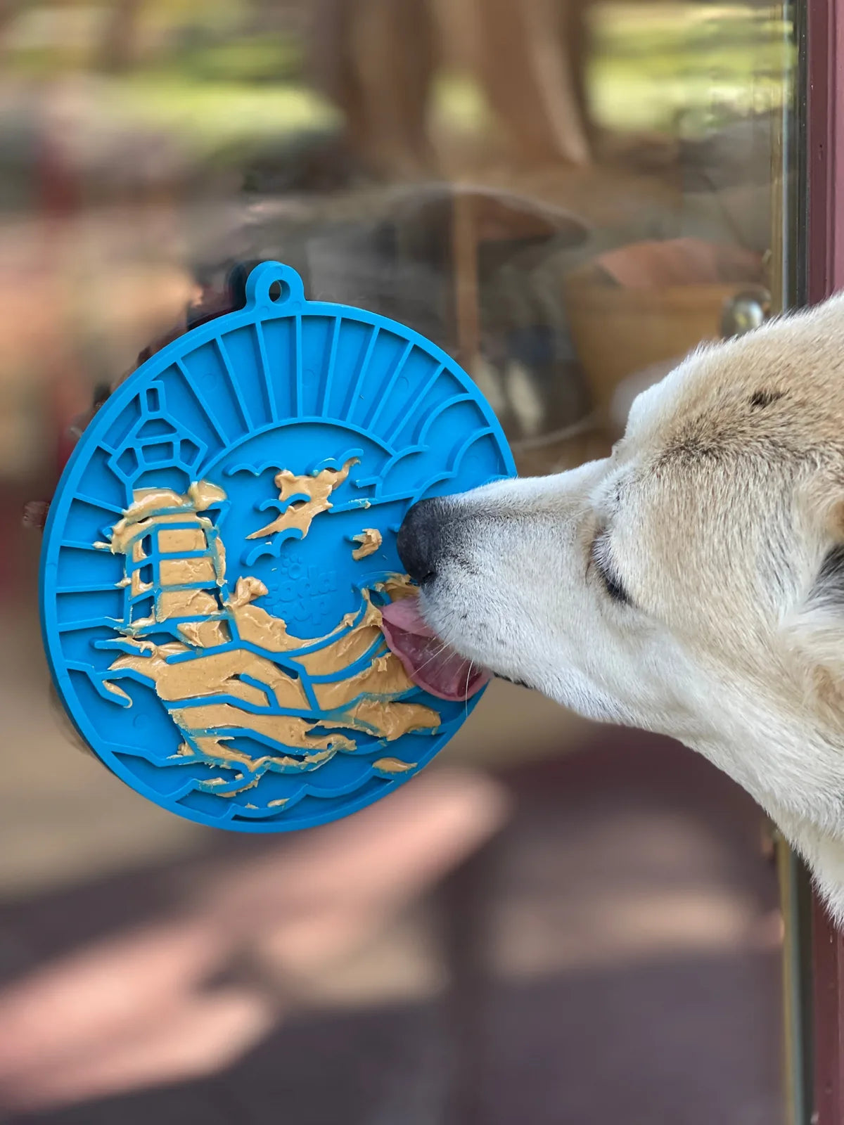 Lighthouse eMat in dark blue with textured surface, securely held by suction cups, as a dog licks spreadable treats.
