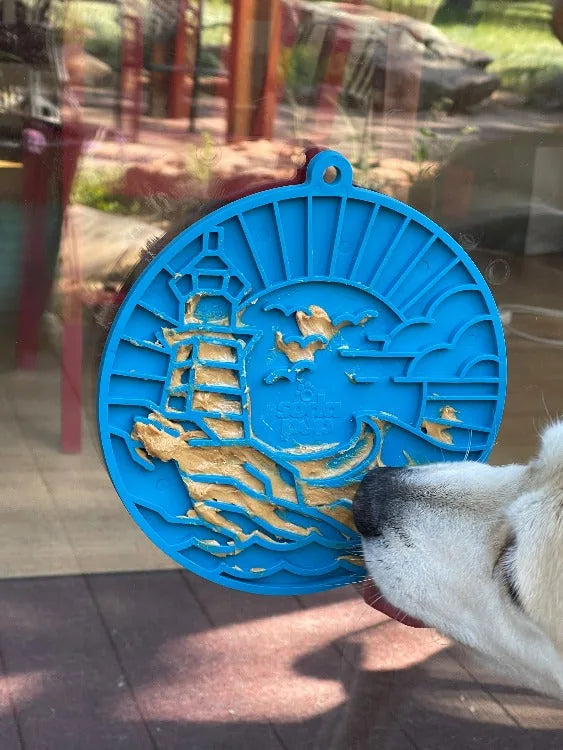 Dark blue lighthouse-shaped enrichment lick mat with treat spread, secured to a smooth surface, as a dog engages with it.