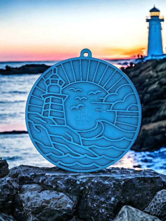 Dark blue lighthouse-shaped enrichment lick mat resting on rocks by the sea, with a sunset backdrop and intricate wave pat...