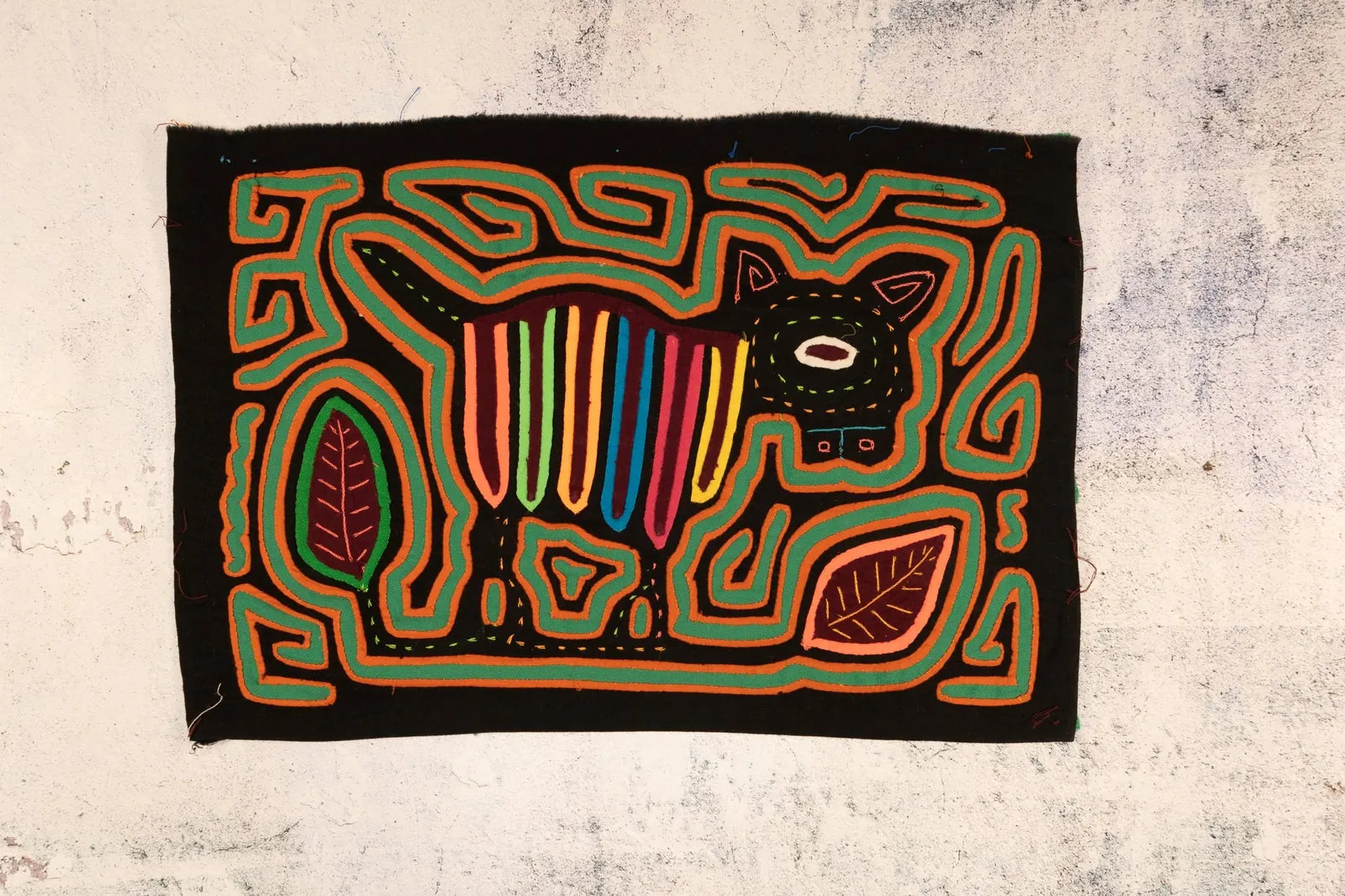 Colorful hand-stitched Mola tapestry featuring a stylized dog against a black background, surrounded by leaves and geometr...