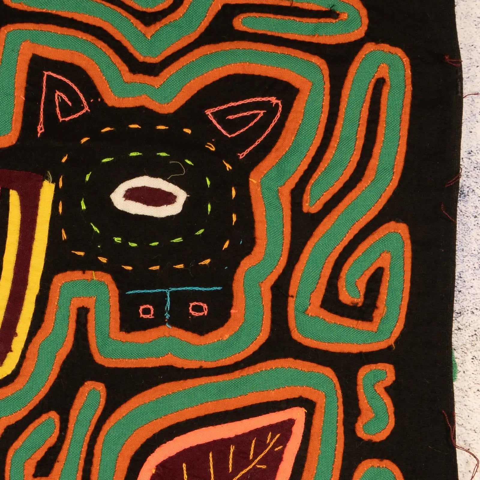 Colorful hand-stitched Mola design featuring a puppy with geometric patterns in vibrant shades on a dark background.