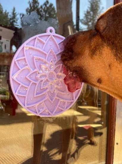 Dog licking a pastel purple lotus design lick mat with suction cups, attached to a window, enhancing snack time engagement.