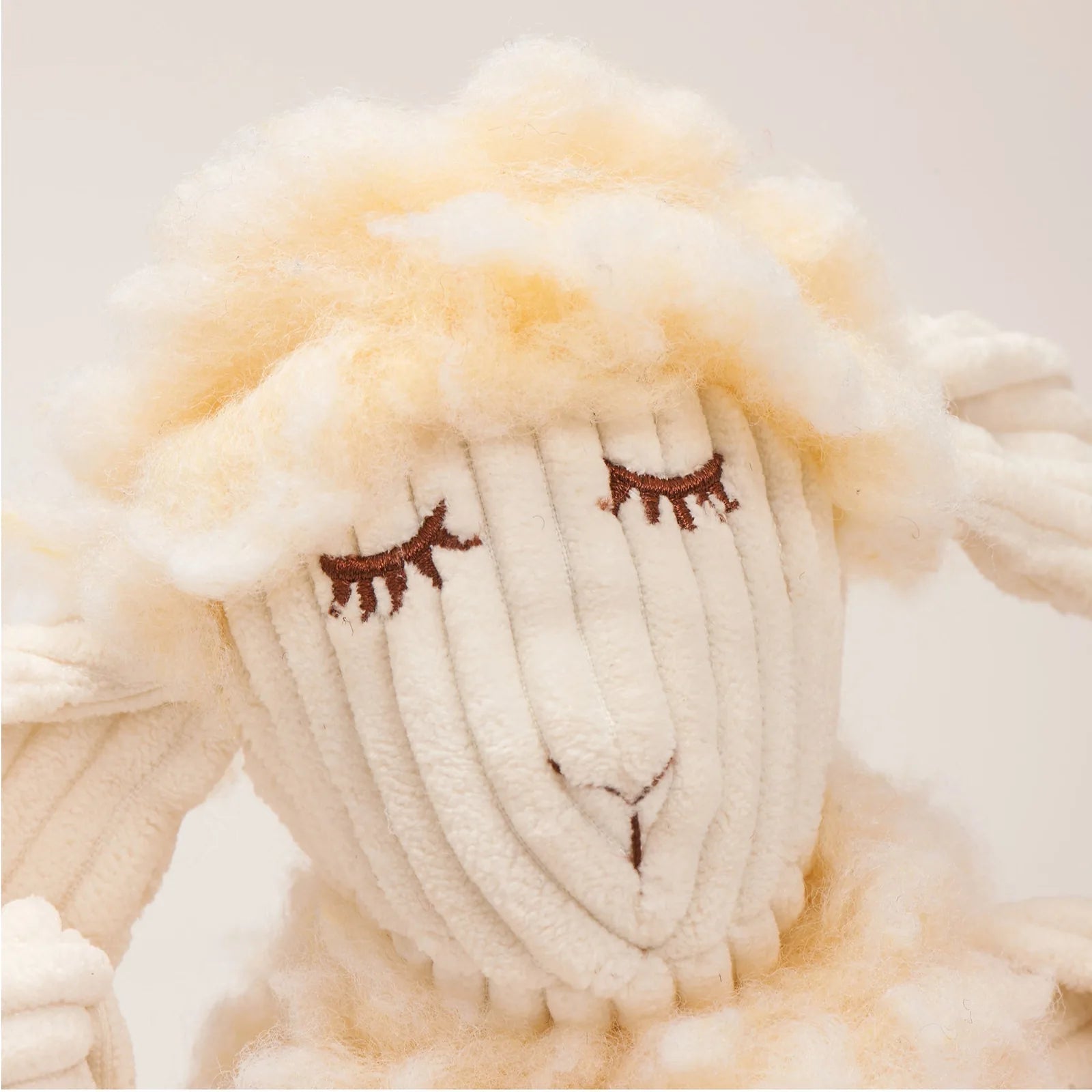 Soft plush lamb toy with closed eyes and fluffy fleece, featuring knotted limbs for interactive play.