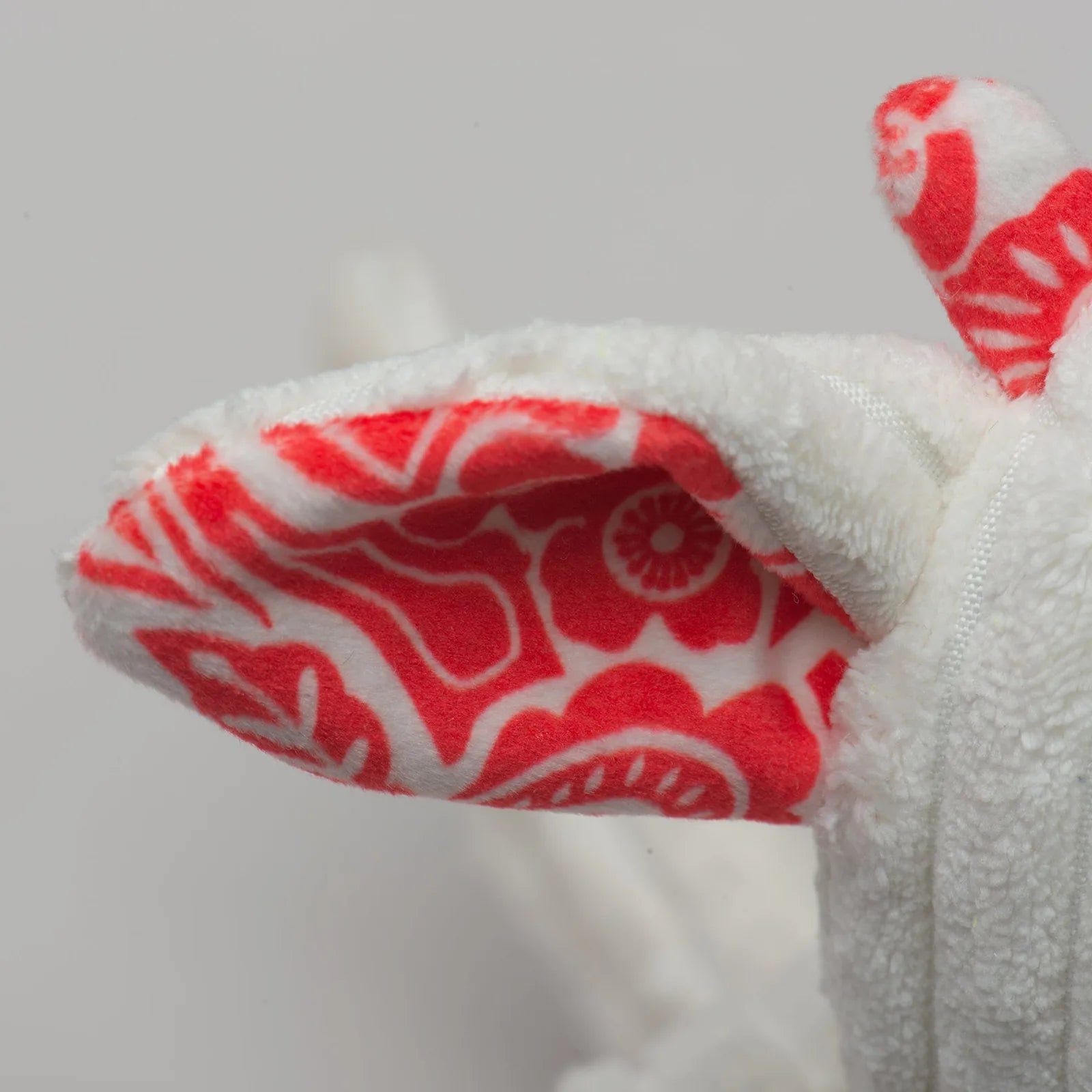Fluffy white plush dog toy ear with a vibrant red floral pattern, designed for interactive play.