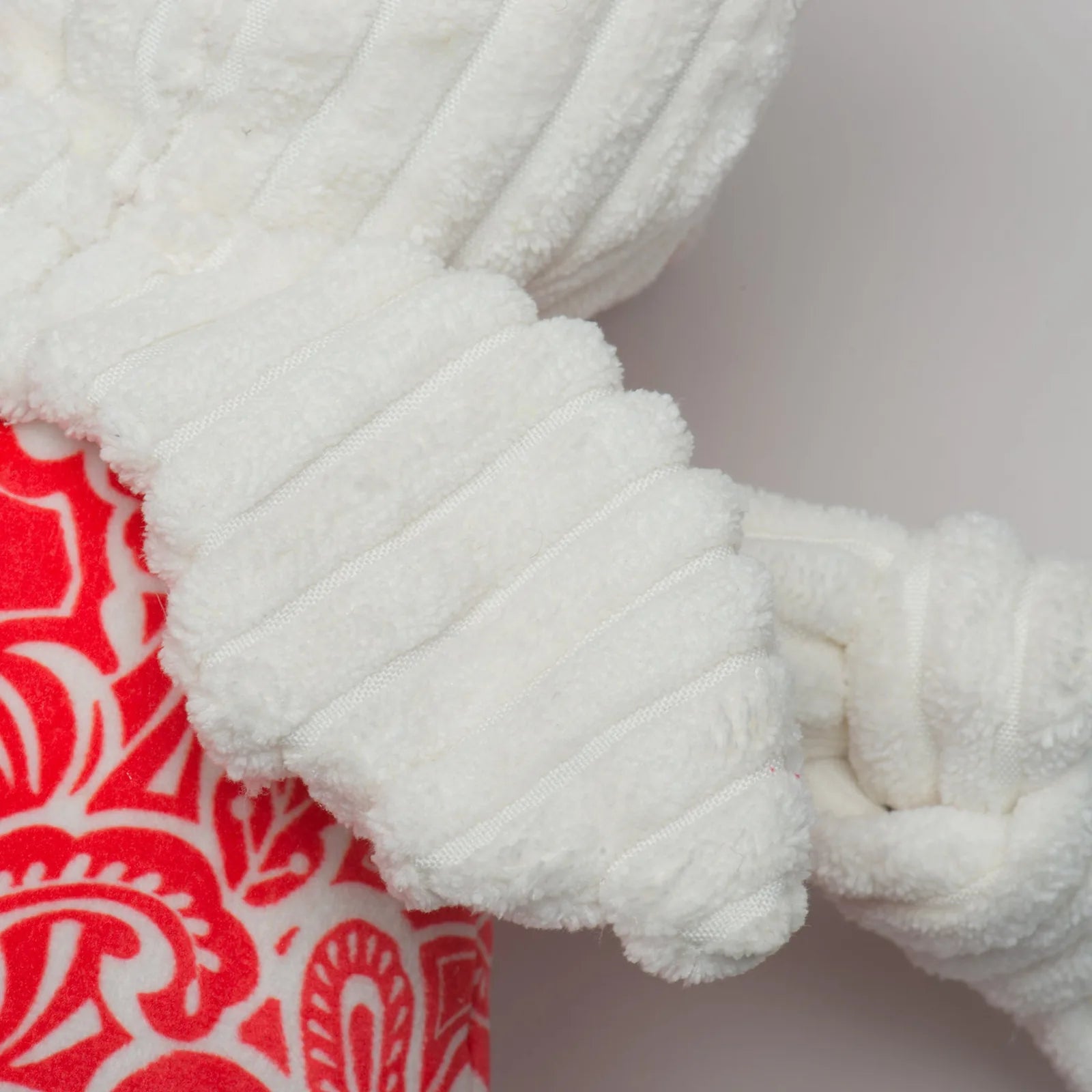 Textured white plush arms grip a red and white patterned body of the Lucky Dragon Knottie® plush dog toy.