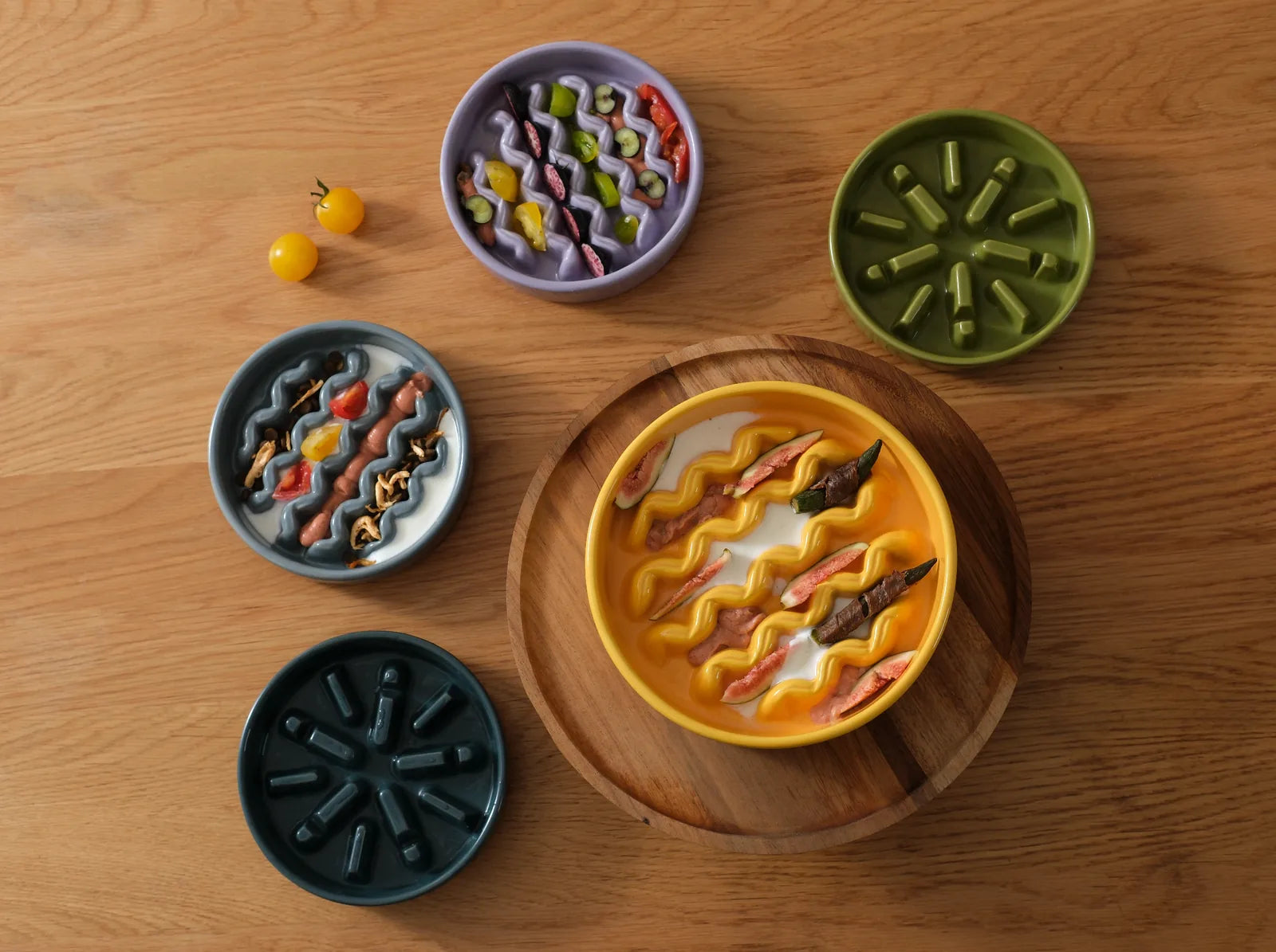 Colorful slow feeder dog bowls in yellow, purple, and blue, featuring wavy designs and placed on wood.