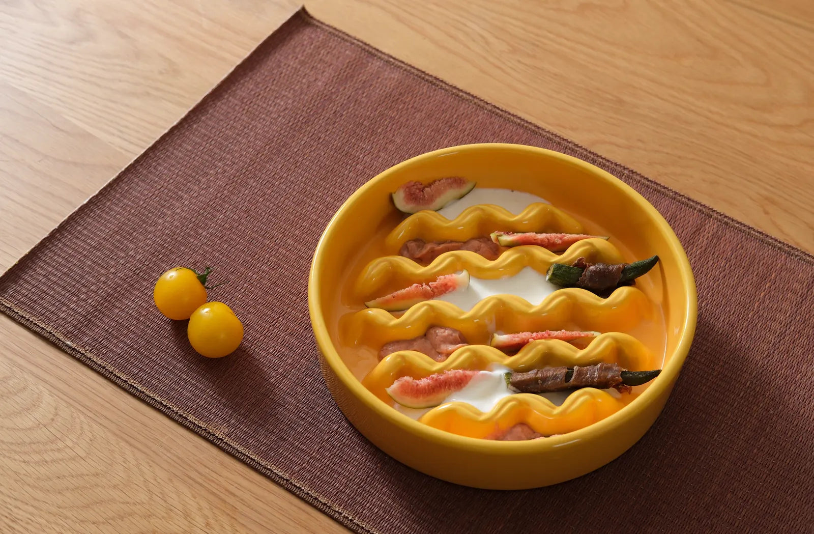 Bright yellow slow feeder dog bowl with wavy design, filled with food and garnished with vegetables, on a brown mat.