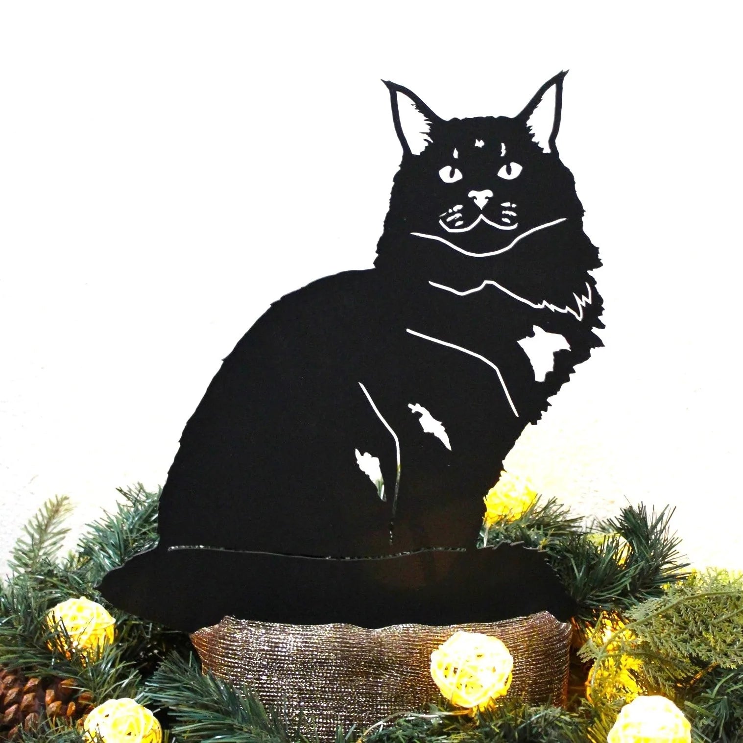 Black Maine Coon metal silhouette sitting among decorative lights and greenery, showcasing handmade outdoor art.