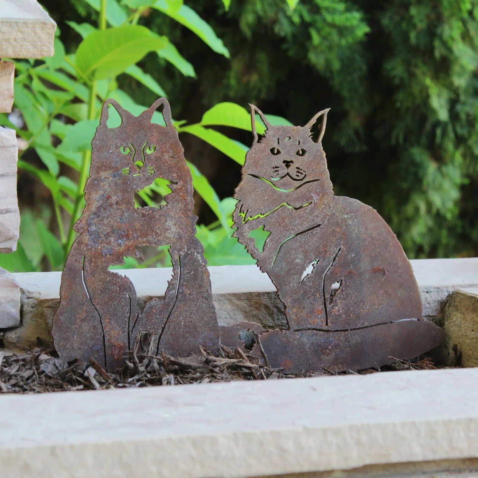 Handmade Maine Coon metal silhouette in weathered Corten steel, featuring two cats sitting among green foliage.