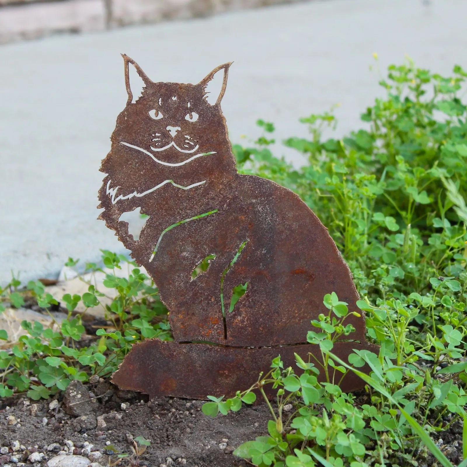 Rusty Maine Coon metal silhouette accenting green ground cover, handmade from weathering steel for outdoor decor.