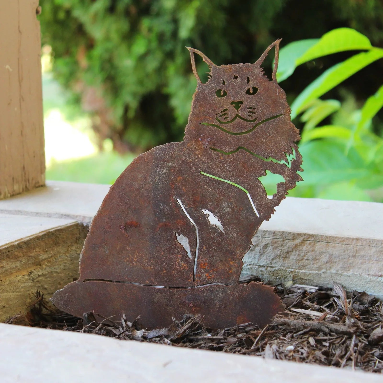 Rusty Corten steel Maine Coon cat silhouette nestled in mulch, perfect for garden decor.