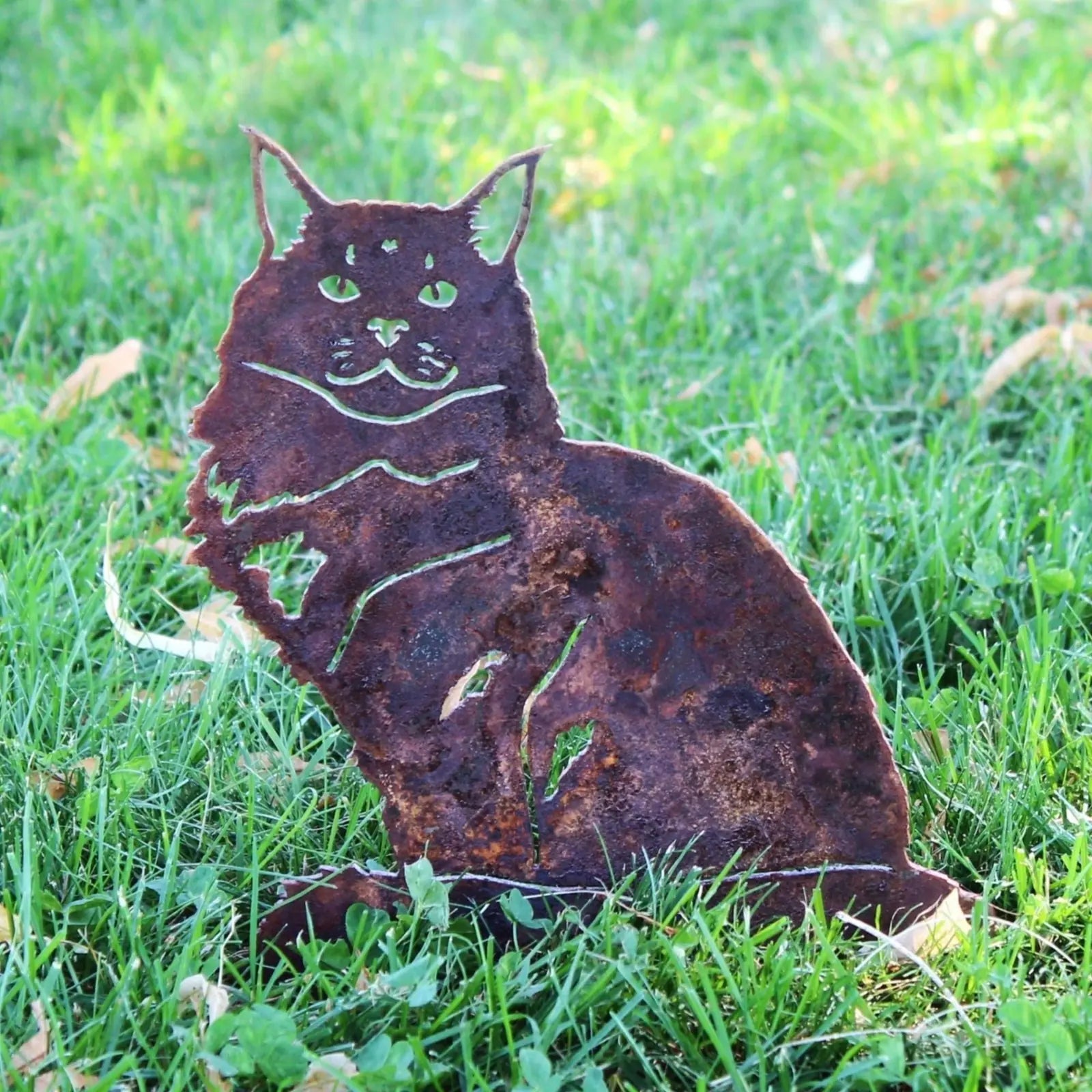Rusty Corten steel silhouette of a Maine Coon cat seated in lush green grass, showcasing intricate handmade details.