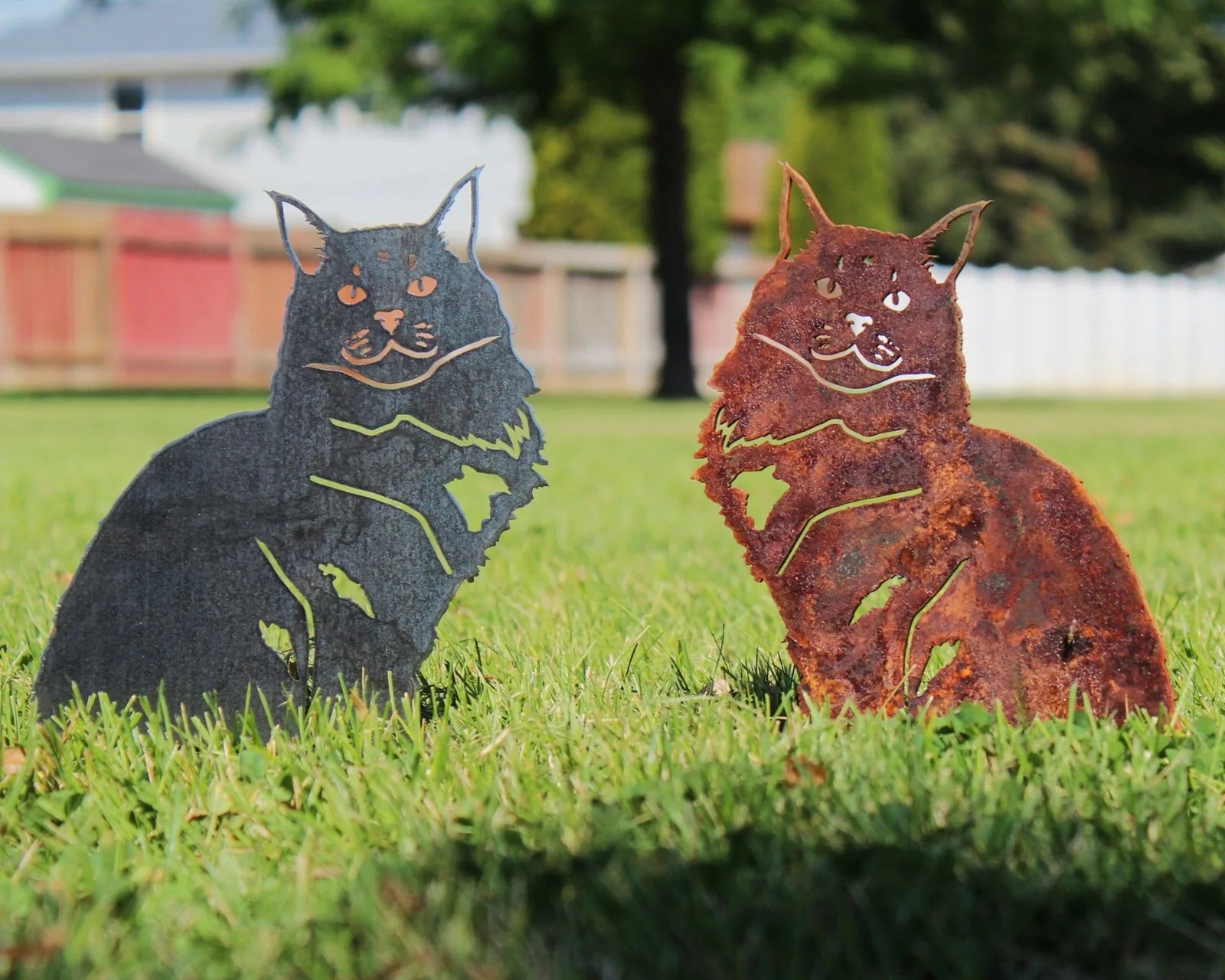 Maine Coon metal silhouettes in matte black and rusted Corten steel, set on vibrant green grass.