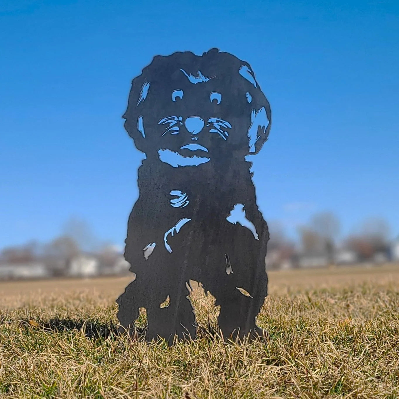 Maltese metal silhouette standing on grass with a clear blue sky backdrop, showcasing its detailed design.